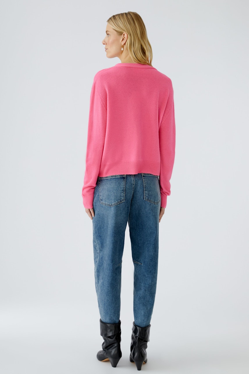 Bequeme Damen-Strickjacke in Pink, lässig kombiniert mit Jeans, zeigt eine Frau von hinten.