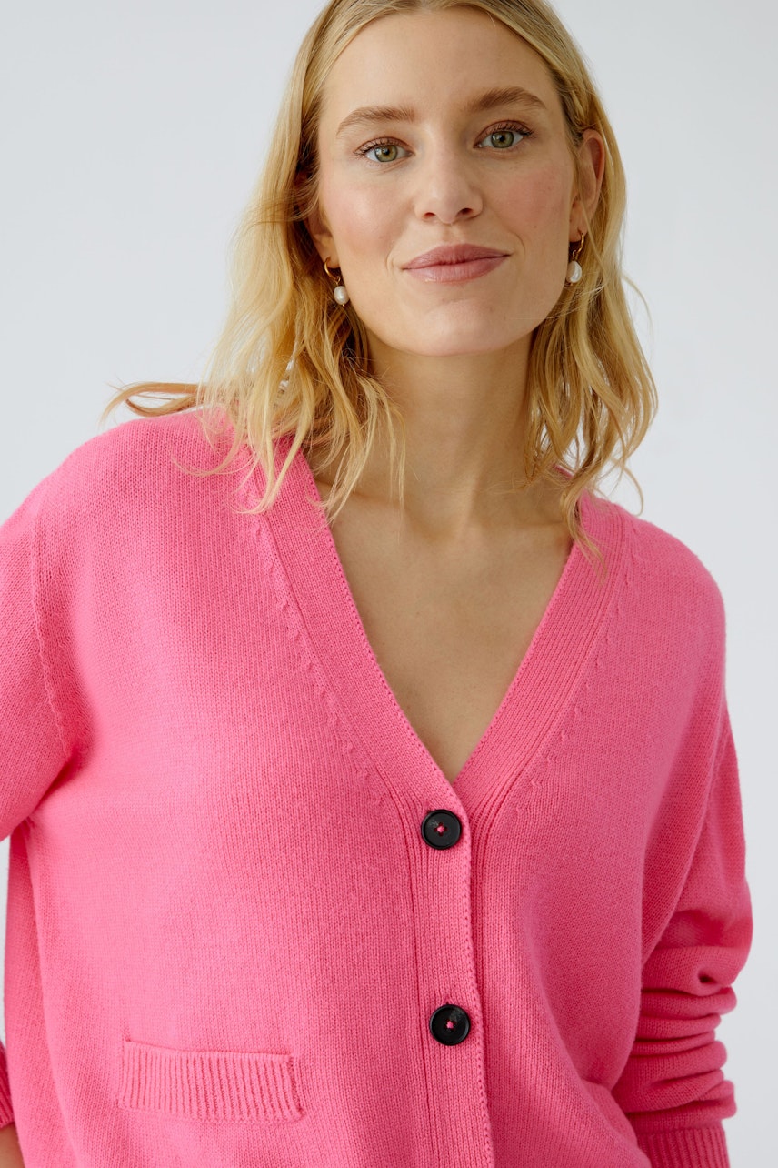 Feminine Strickjacke in leuchtendem Pink mit V-Ausschnitt und Knöpfen, lässig getragen von einer Frau.