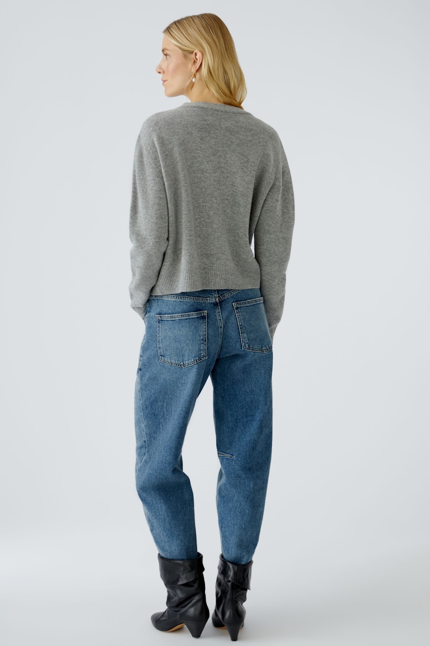 Damen-Strickjacke: Frau in grauer Strickjacke mit lässigem Schnitt und bequemen Jeans von hinten.