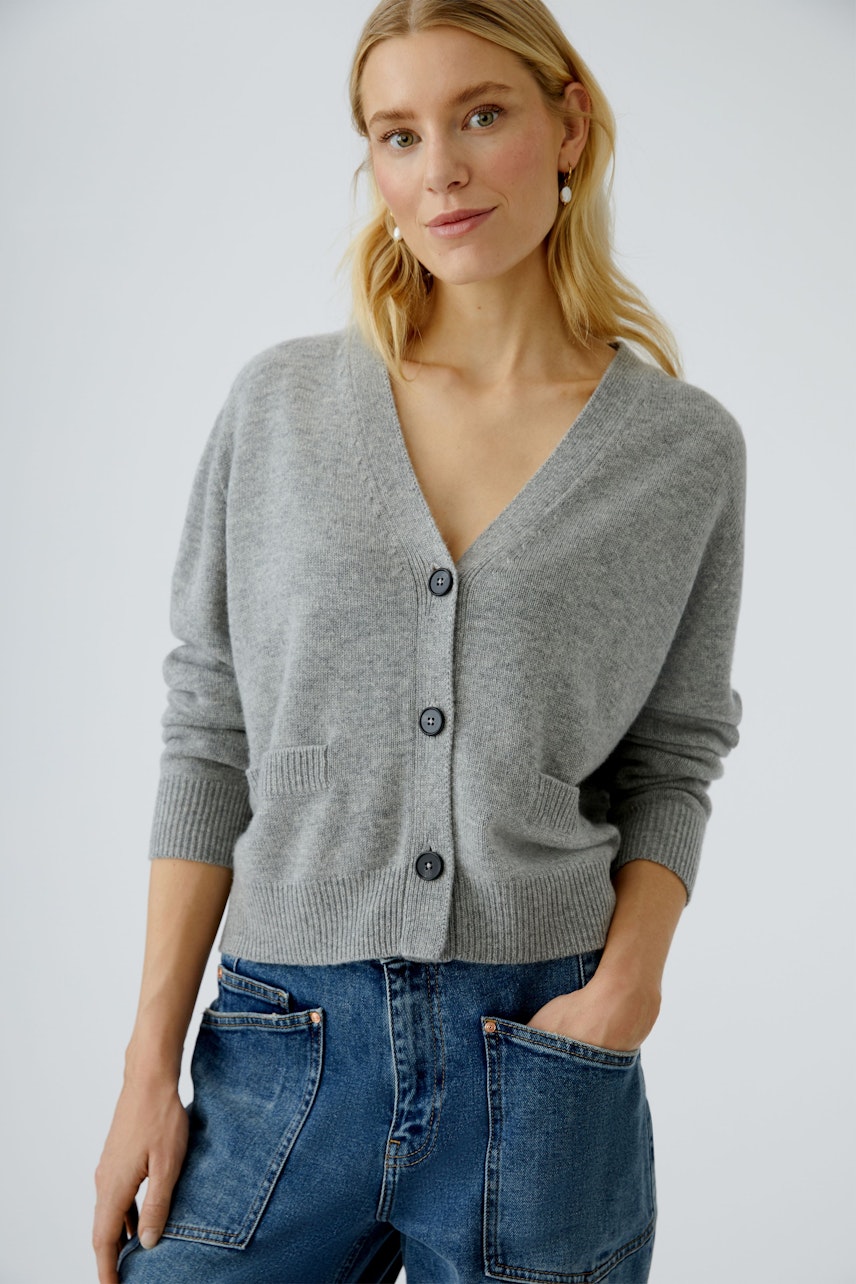 Bequeme Damen-Strickjacke: Frau in grauer Strickjacke mit V-Ausschnitt und Taschen, lässig in Jeans.