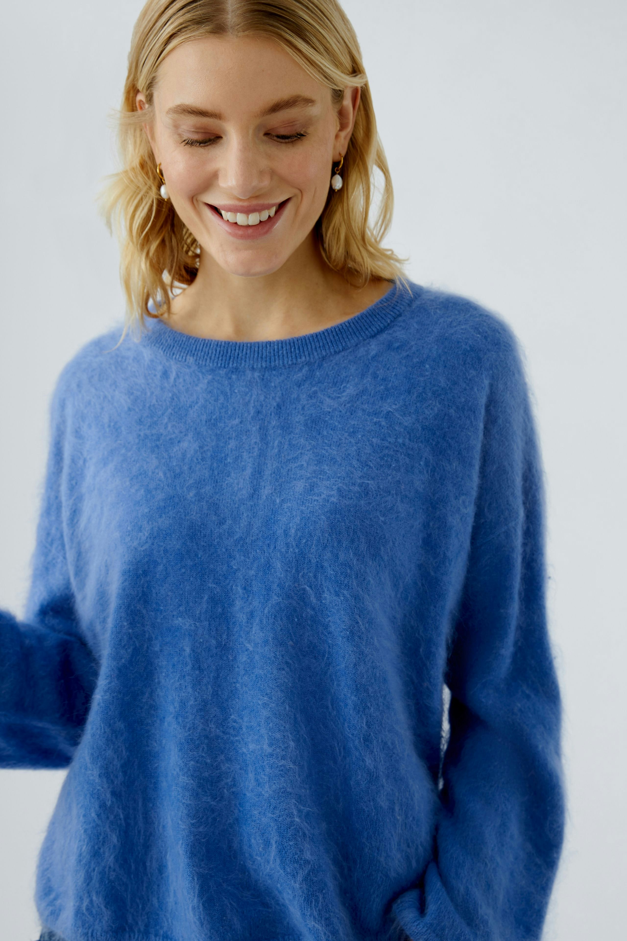 Casual women's pullover: Smiling woman in a soft blue pullover, showcasing a relaxed style.