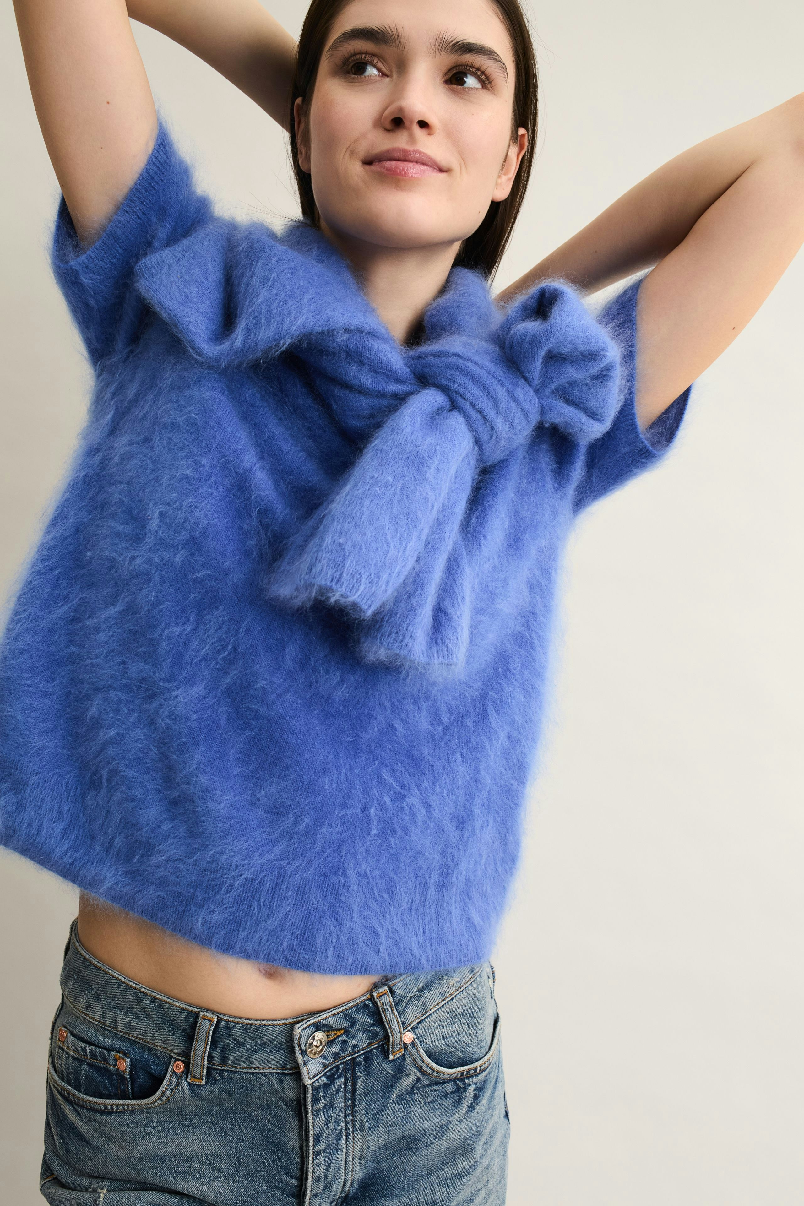 Casual women's pullover: Young woman in a fluffy blue pullover with a bow detail, smiling and relaxed.