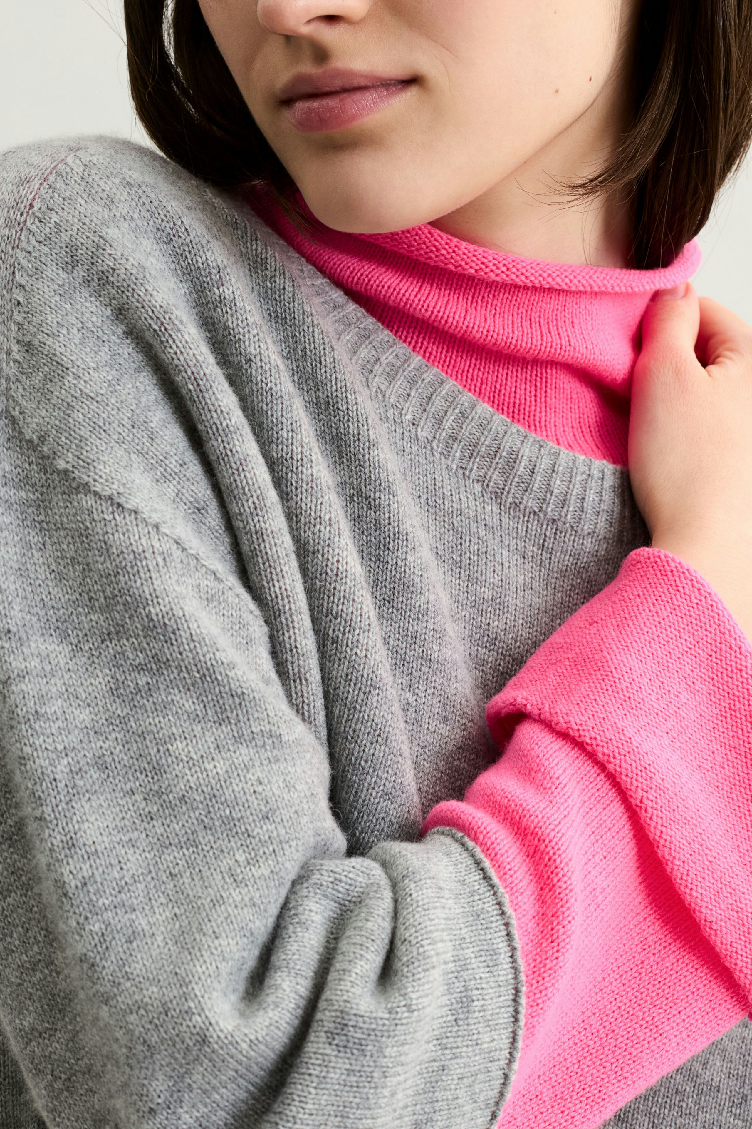 Casual women's pullover: Young woman in a gray pullover layered over a bright pink top.
