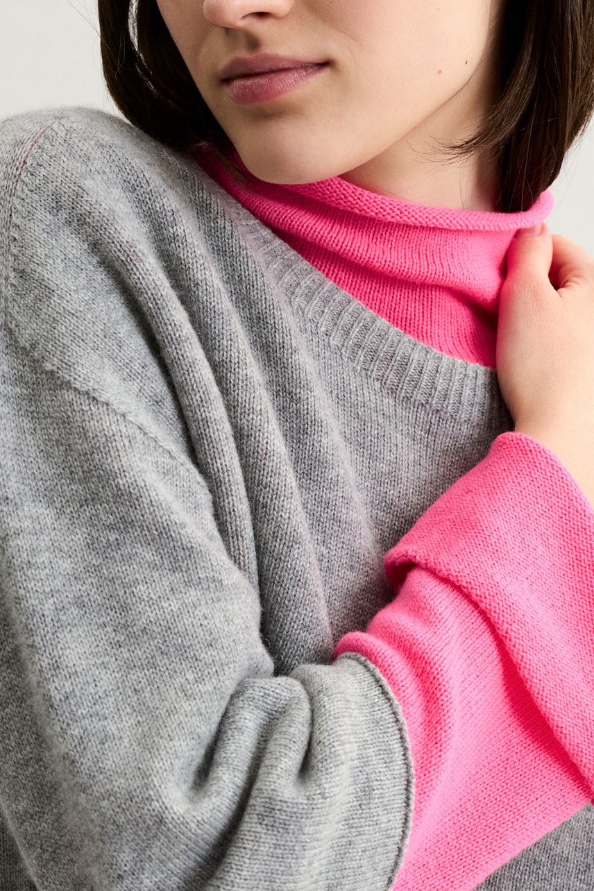 Casual women's pullover: Young woman in a gray pullover layered over a bright pink top.