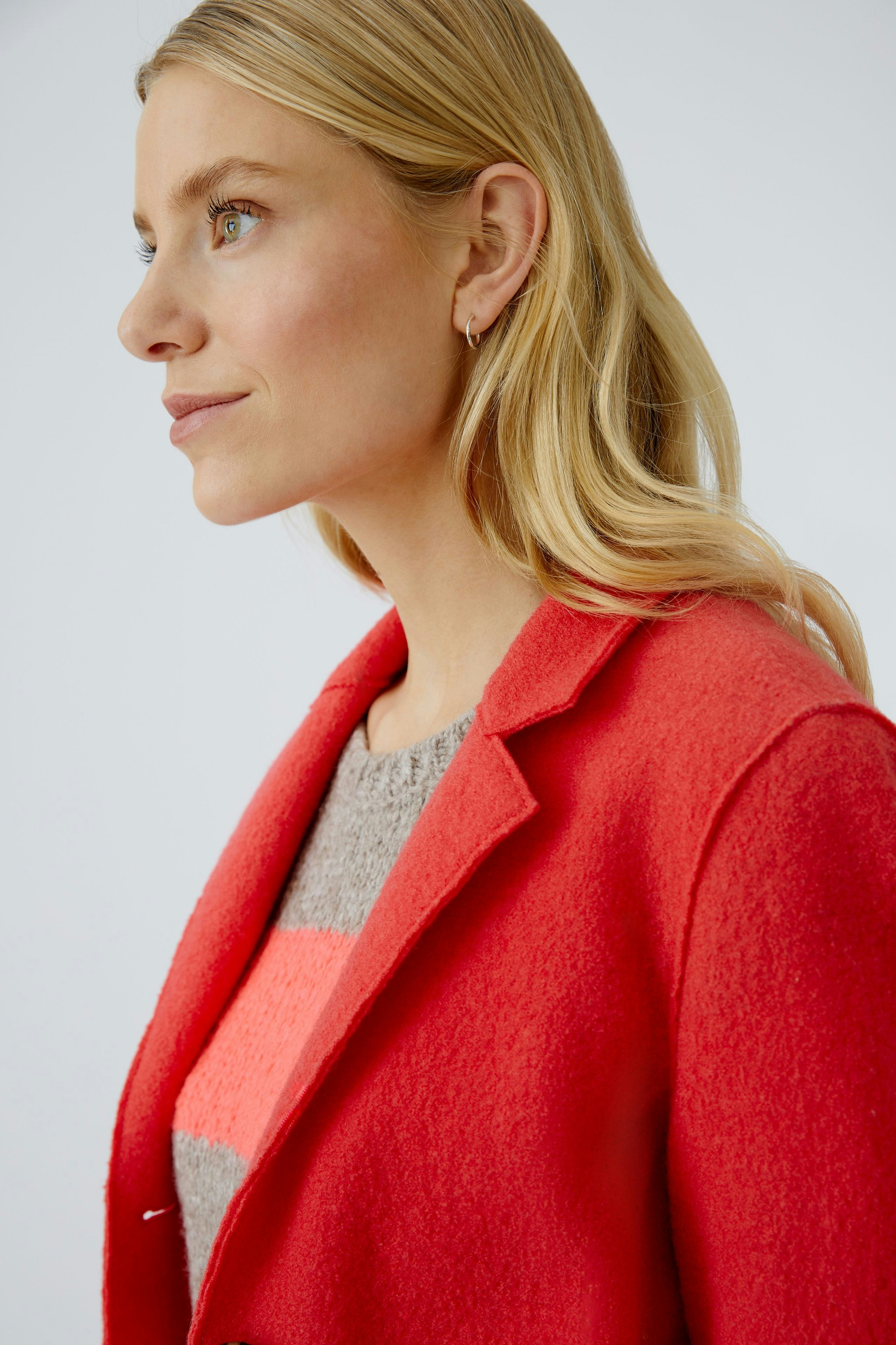 Wollmantel: Frau trägt einen roten Wollmantel über einem bunten Pullover.