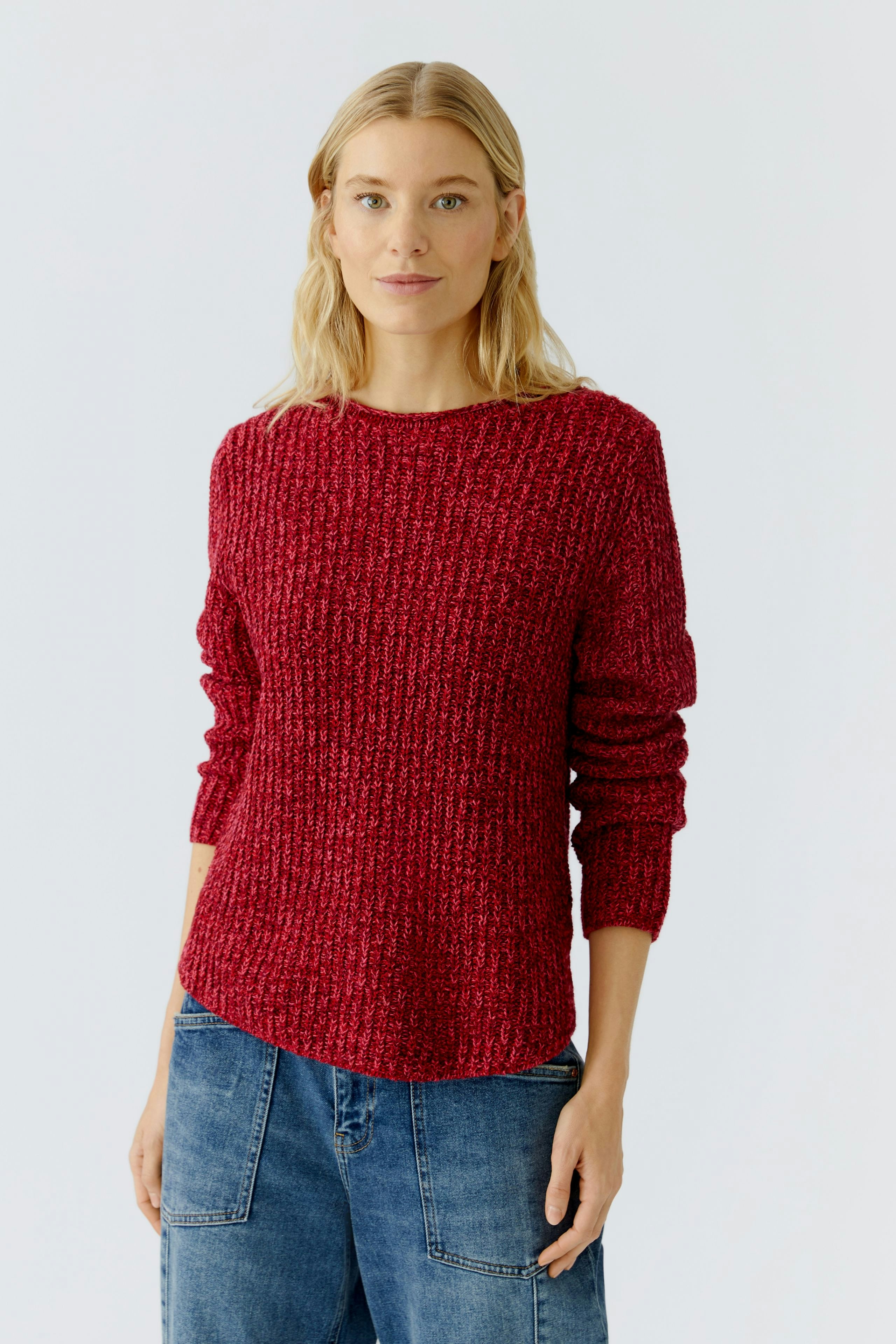 Casual women's pullover: A woman in a red textured pullover paired with relaxed denim jeans.