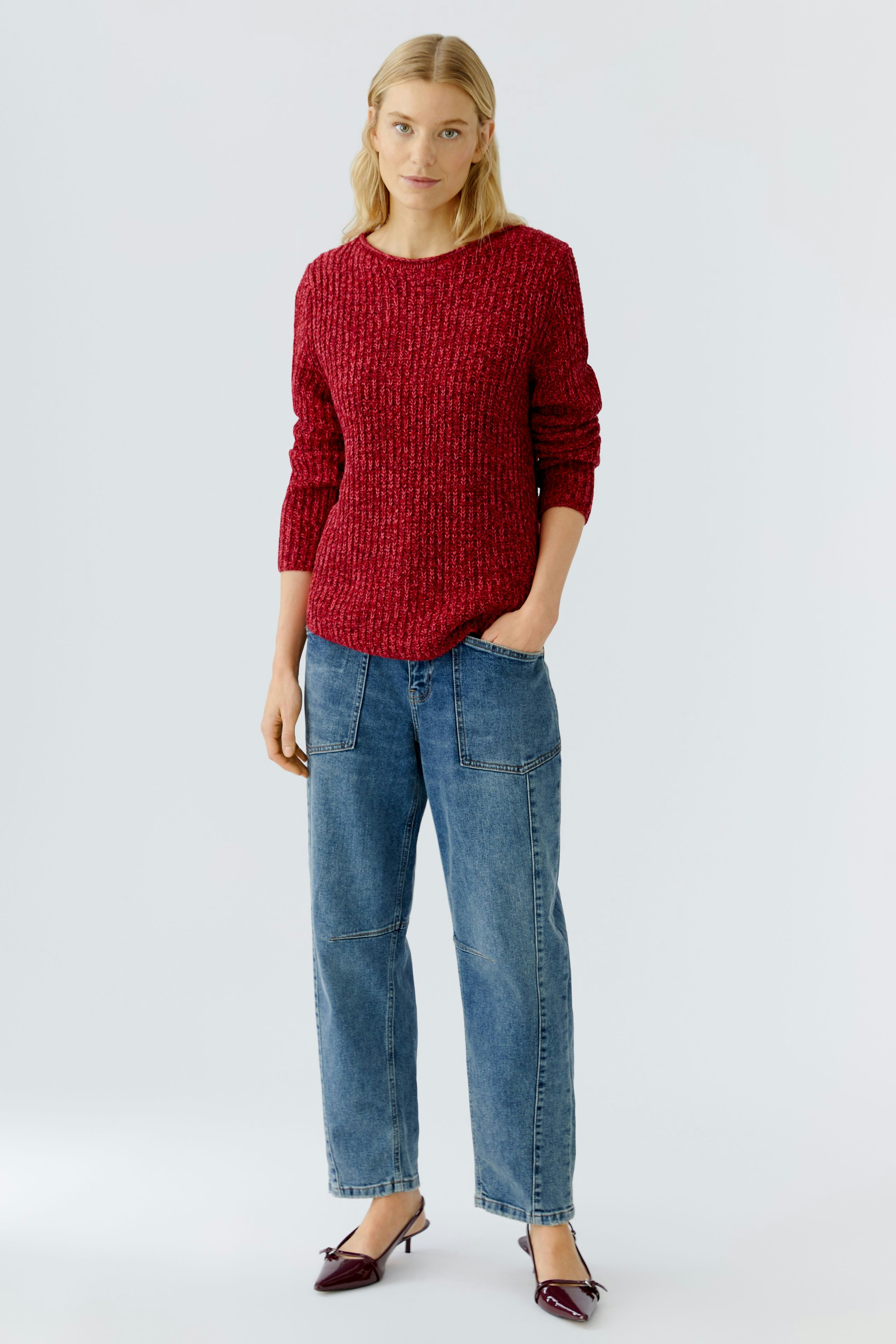 Casual women's pullover: Young woman in a red textured pullover paired with relaxed denim pants.