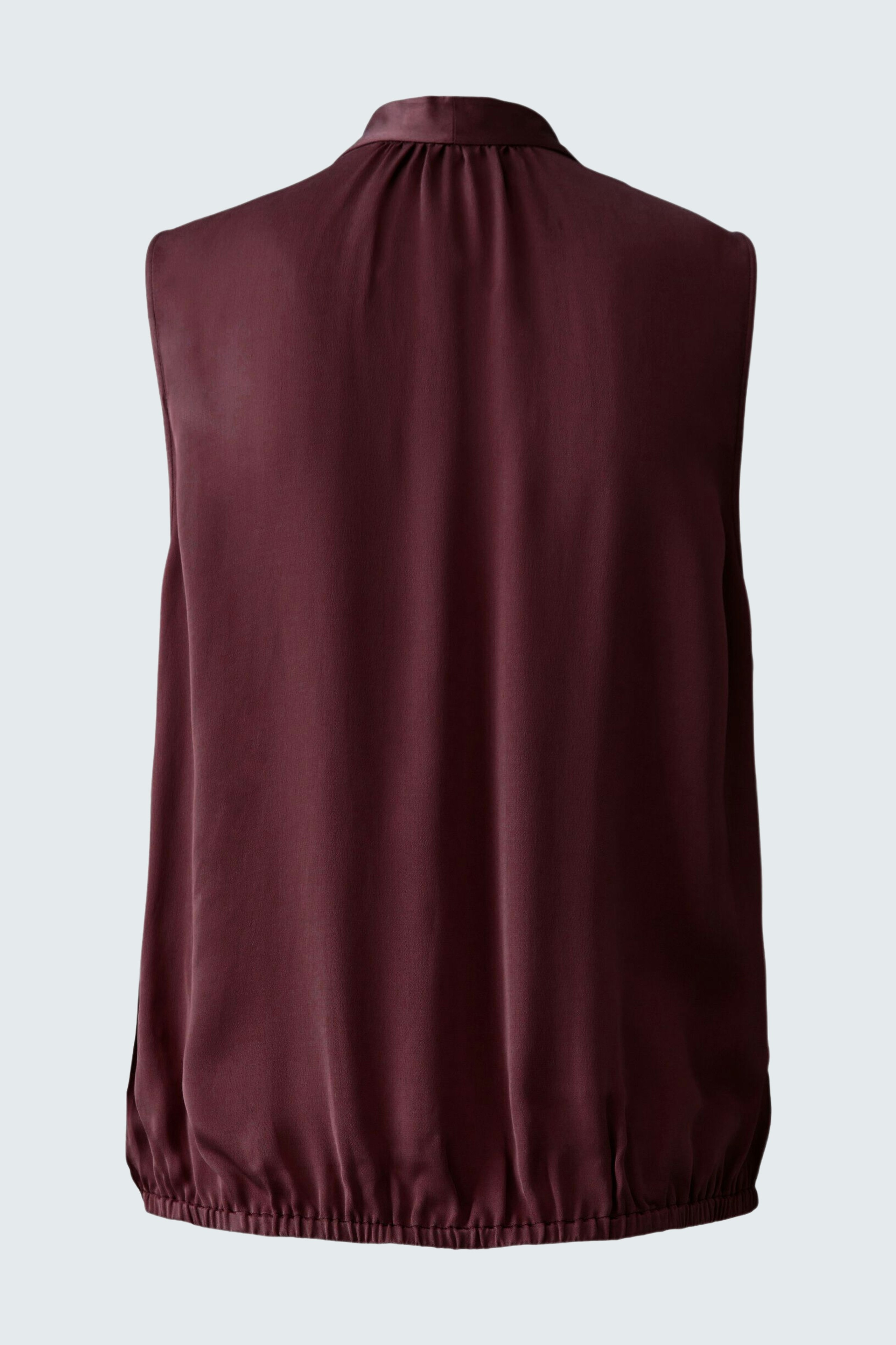 Sleeveless blouse: A woman in a burgundy sleeveless blouse with a gathered hem, showcasing a relaxed style.