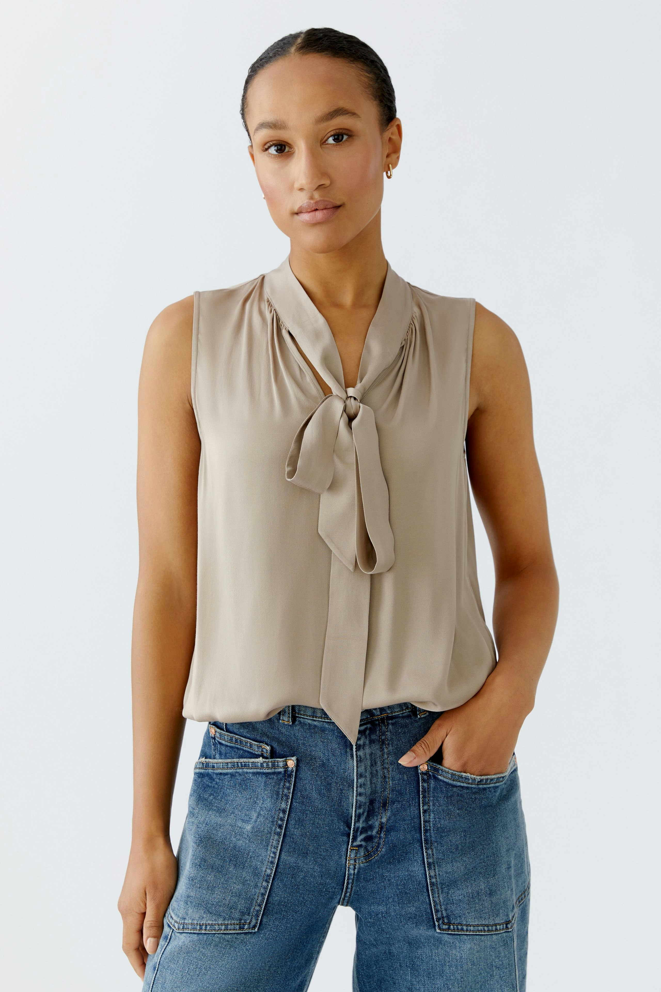 Sleeveless blouse: Woman in a beige blouse with a bow detail, paired with casual denim jeans.