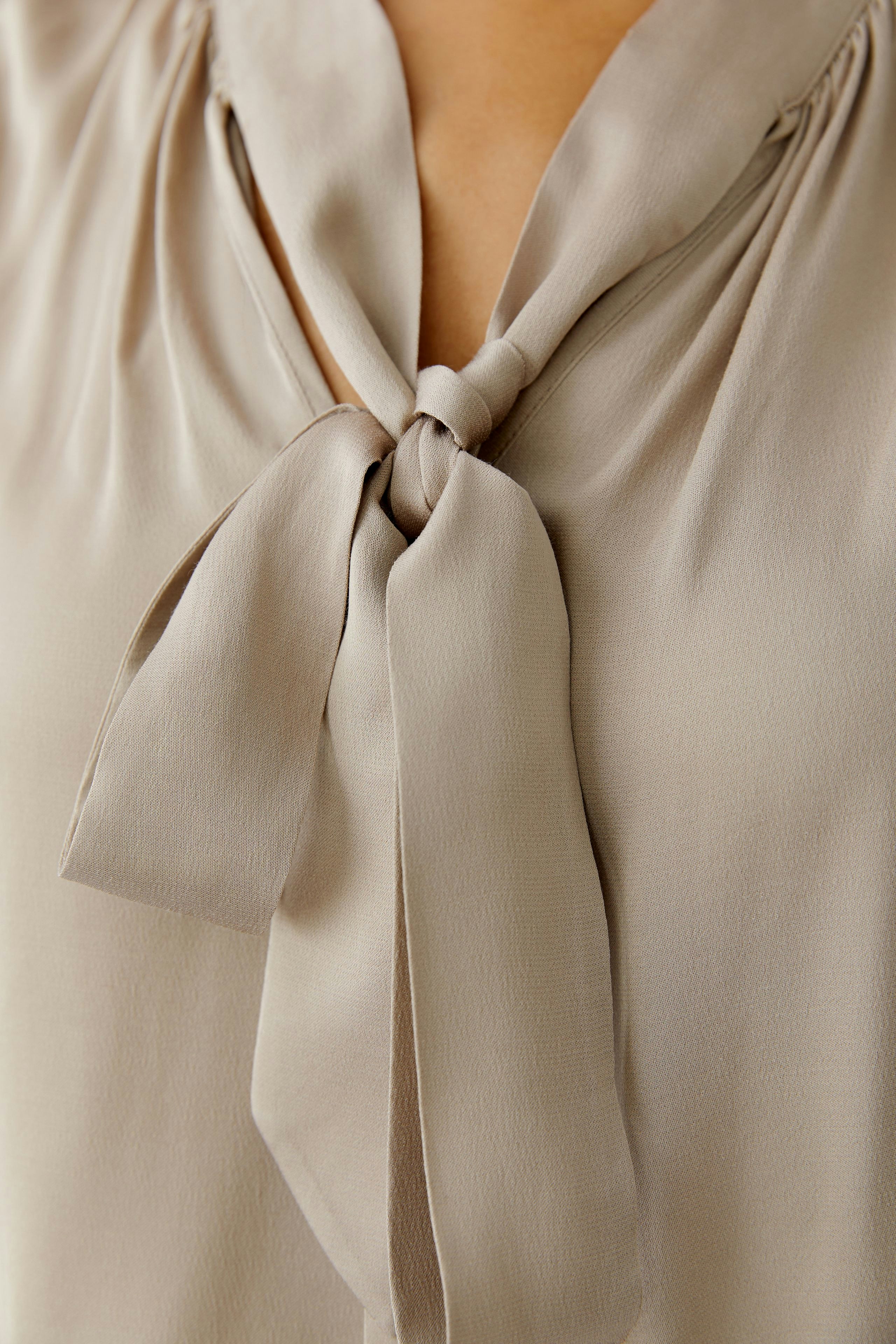 Light beige blouse with a tie detail, worn by a woman, perfect for casual outings.