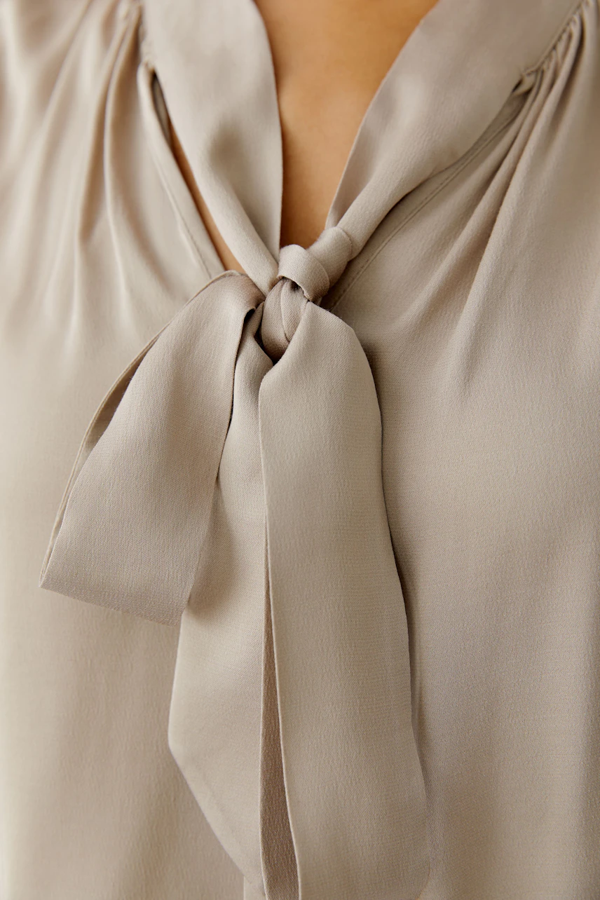 Light beige blouse with a tie detail, worn by a woman, perfect for casual outings.