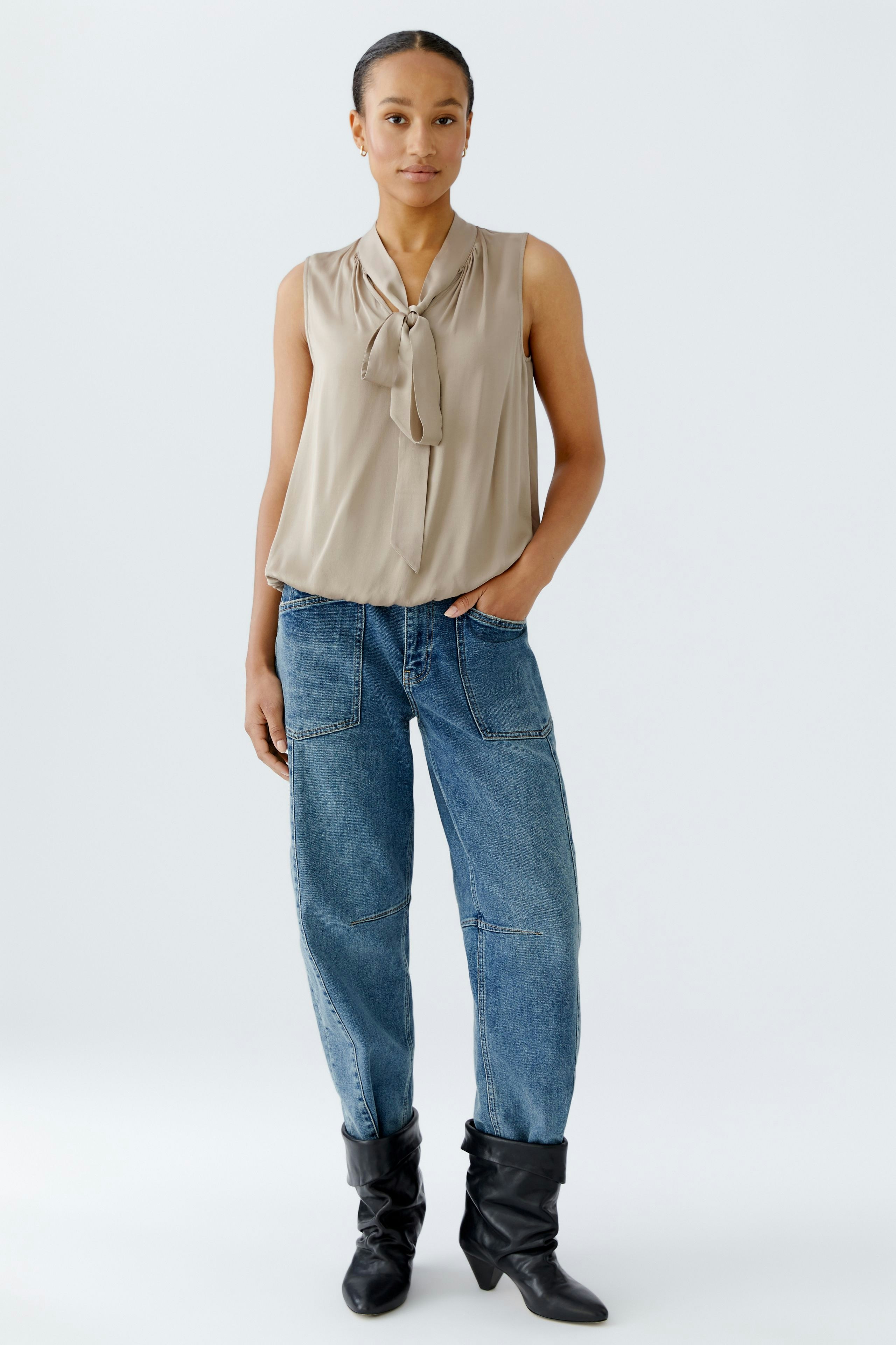 Light blouse with a bow detail: Woman wearing a sleeveless beige blouse paired with relaxed-fit jeans.