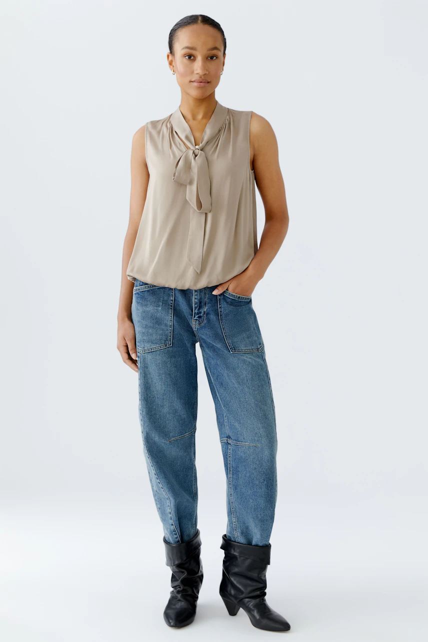 Light blouse with a bow detail: Woman wearing a sleeveless beige blouse paired with relaxed-fit jeans.
