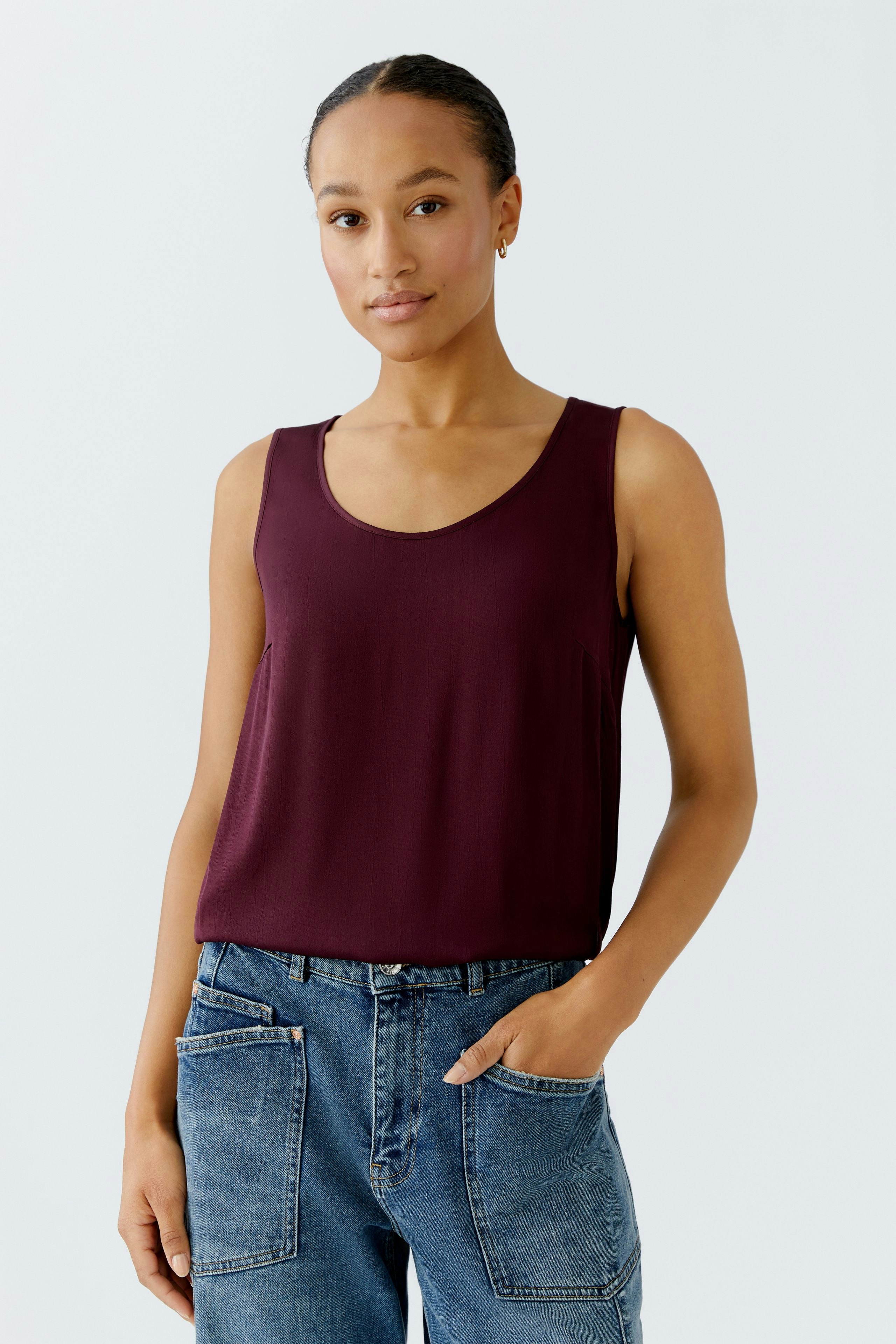 Casual women's top: A woman in a burgundy sleeveless top paired with relaxed-fit jeans.