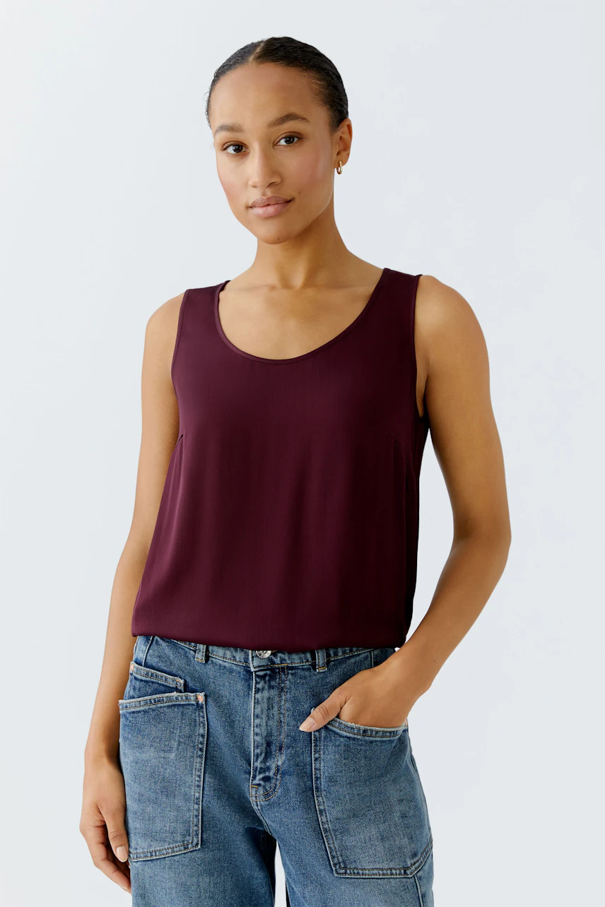 Casual women's top: A woman in a burgundy sleeveless top paired with relaxed-fit jeans.