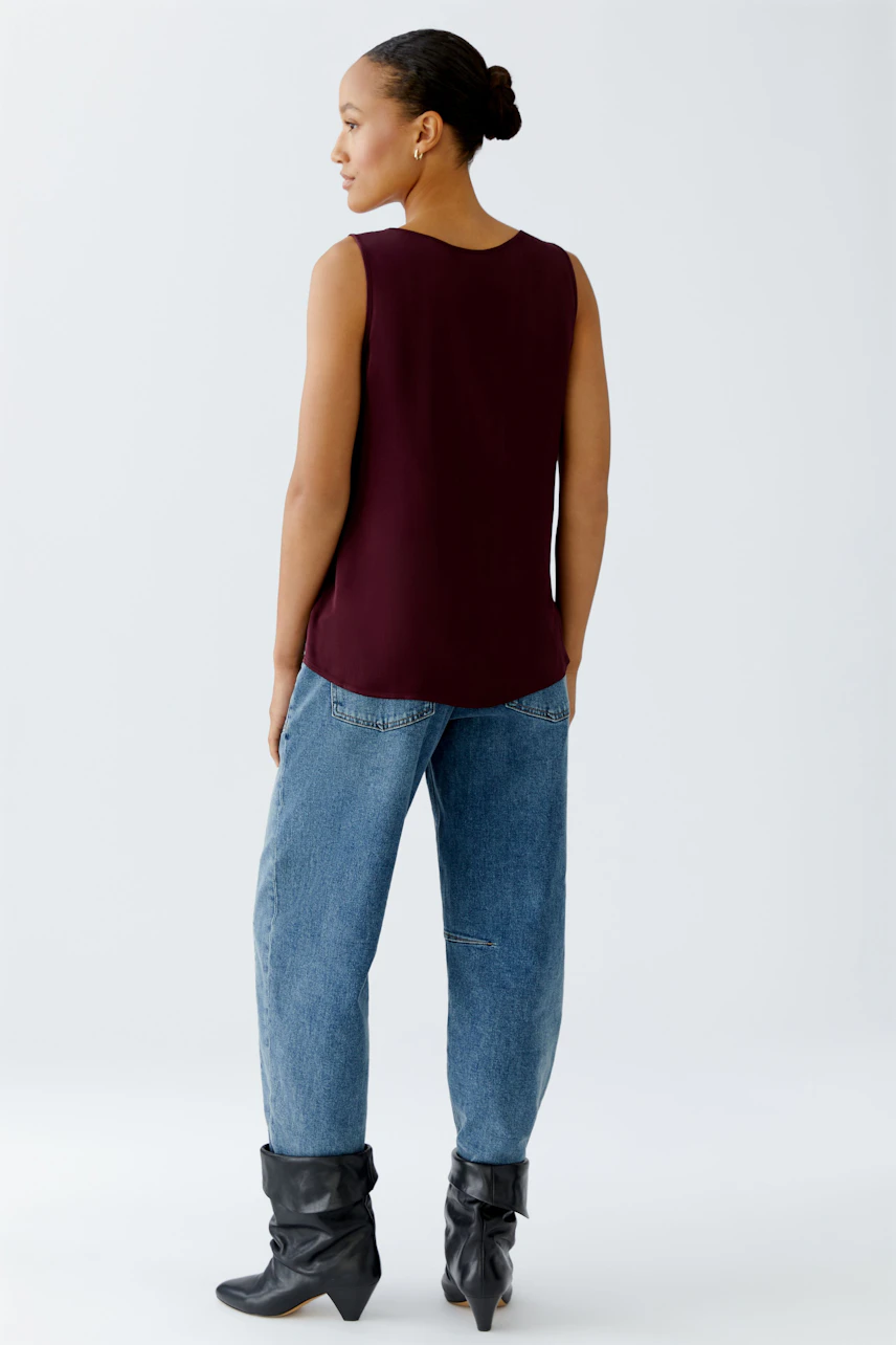 Casual women's top: A woman in a burgundy sleeveless top paired with relaxed jeans.
