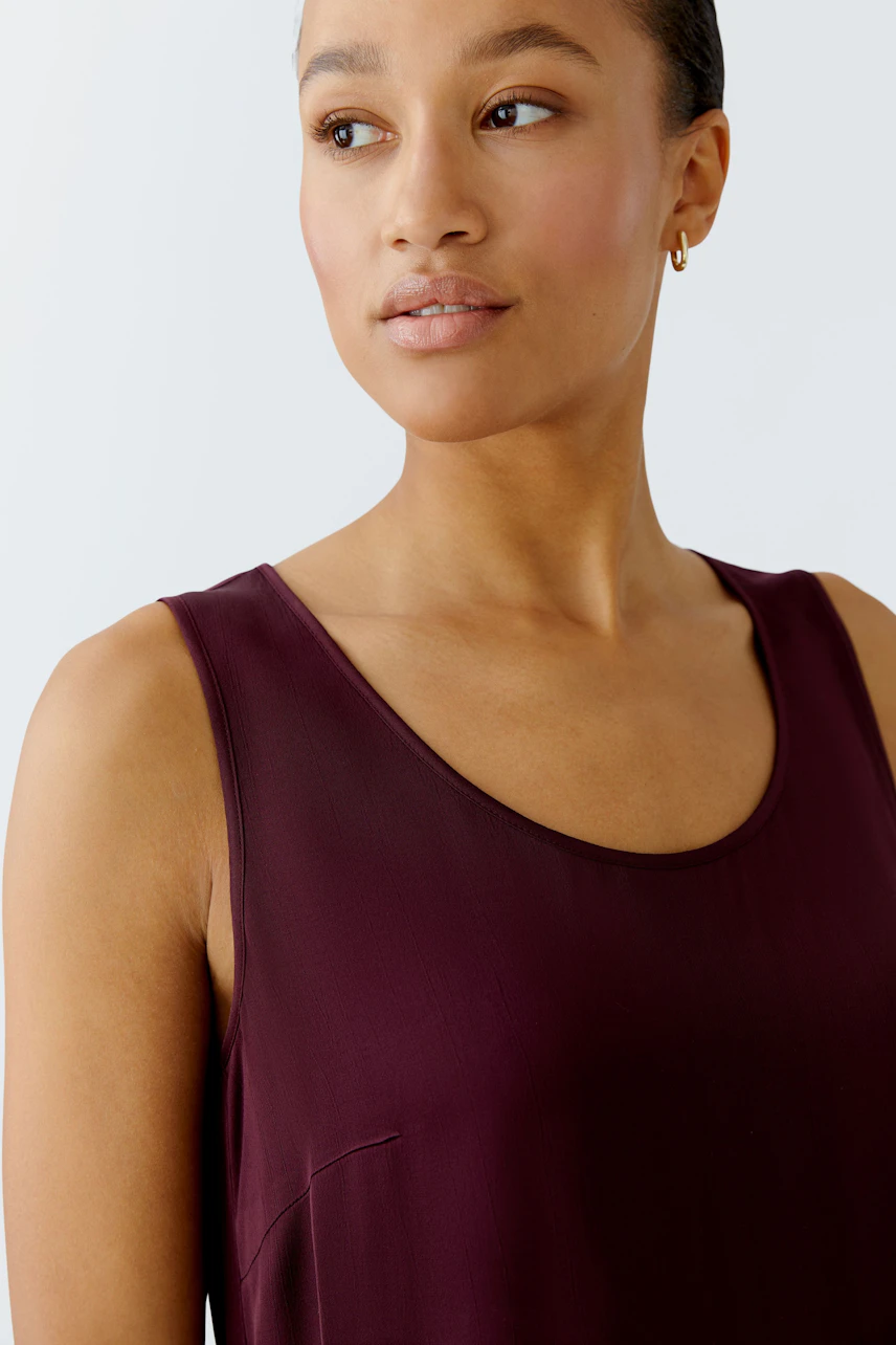 Casual women's top: A woman in a burgundy sleeveless top with a relaxed fit, showcasing a simple design.