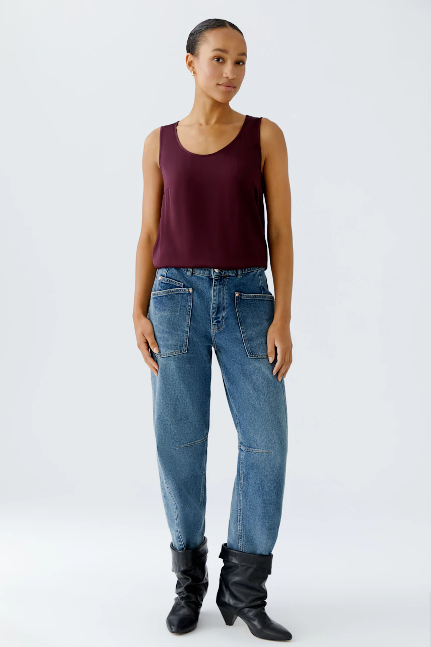 Casual women's top: A woman in a burgundy sleeveless top paired with relaxed-fit jeans.