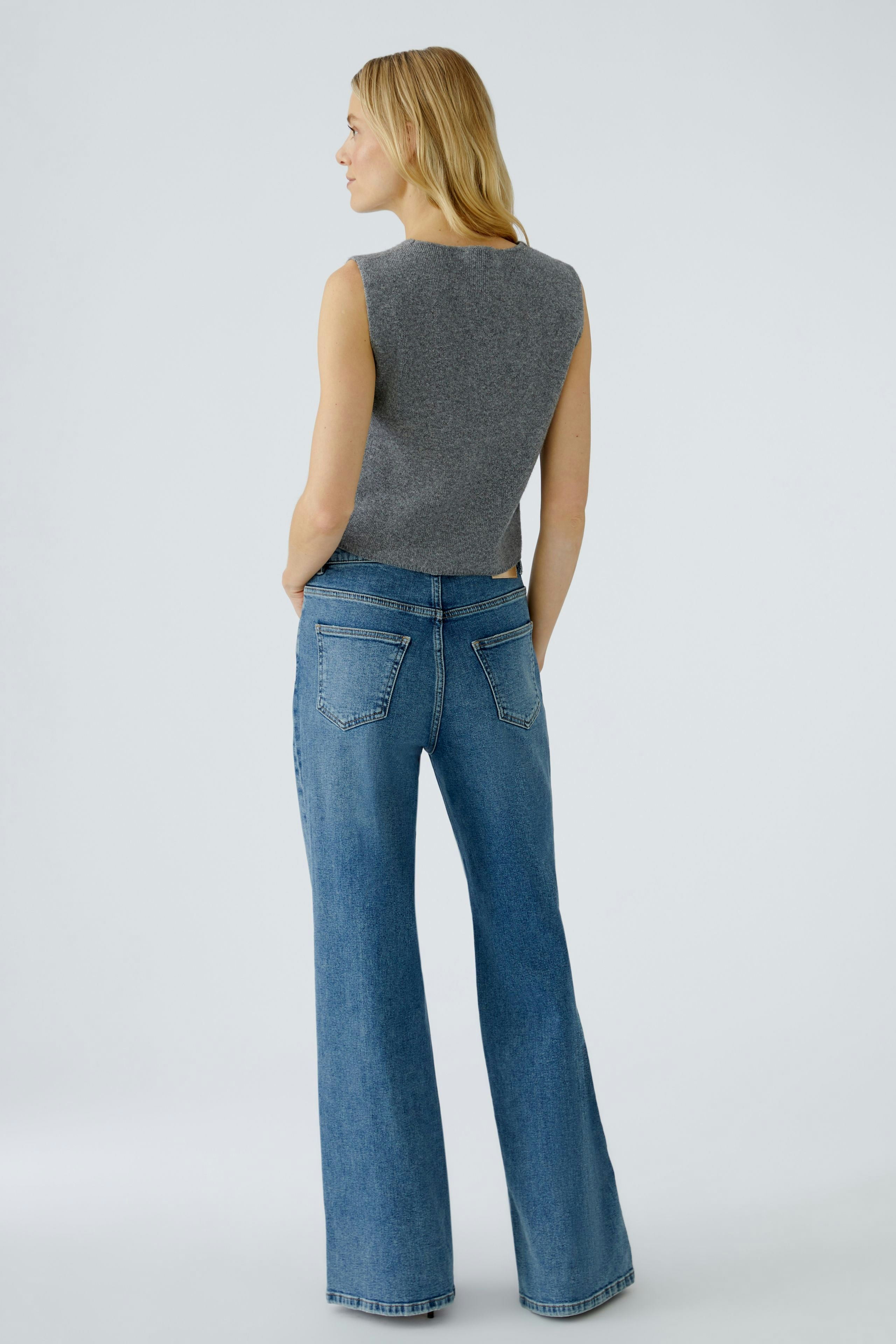 Damen-Strickweste: Frau mit ärmelloser grauer Weste und lässigen Jeans von hinten.