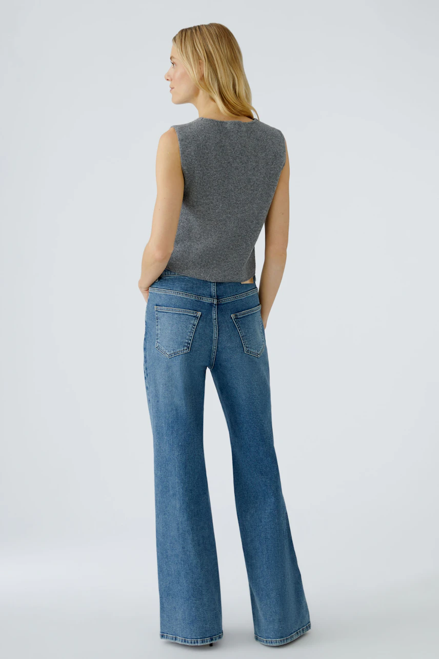 Casual women's cardigan: Young woman in a gray knitted vest paired with flared jeans, showcasing a relaxed style.