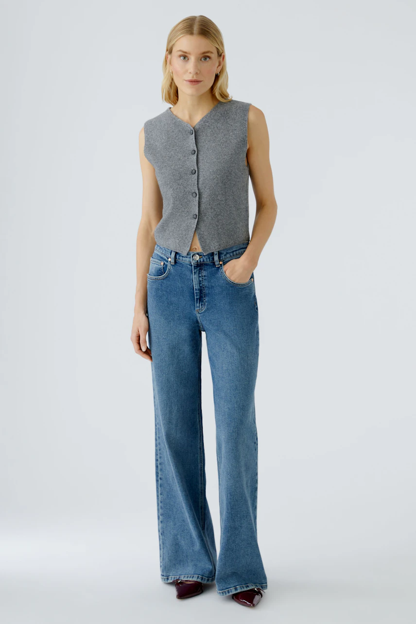 Casual women's cardigan: A woman in a gray sleeveless cardigan with buttons, paired with wide-leg jeans.