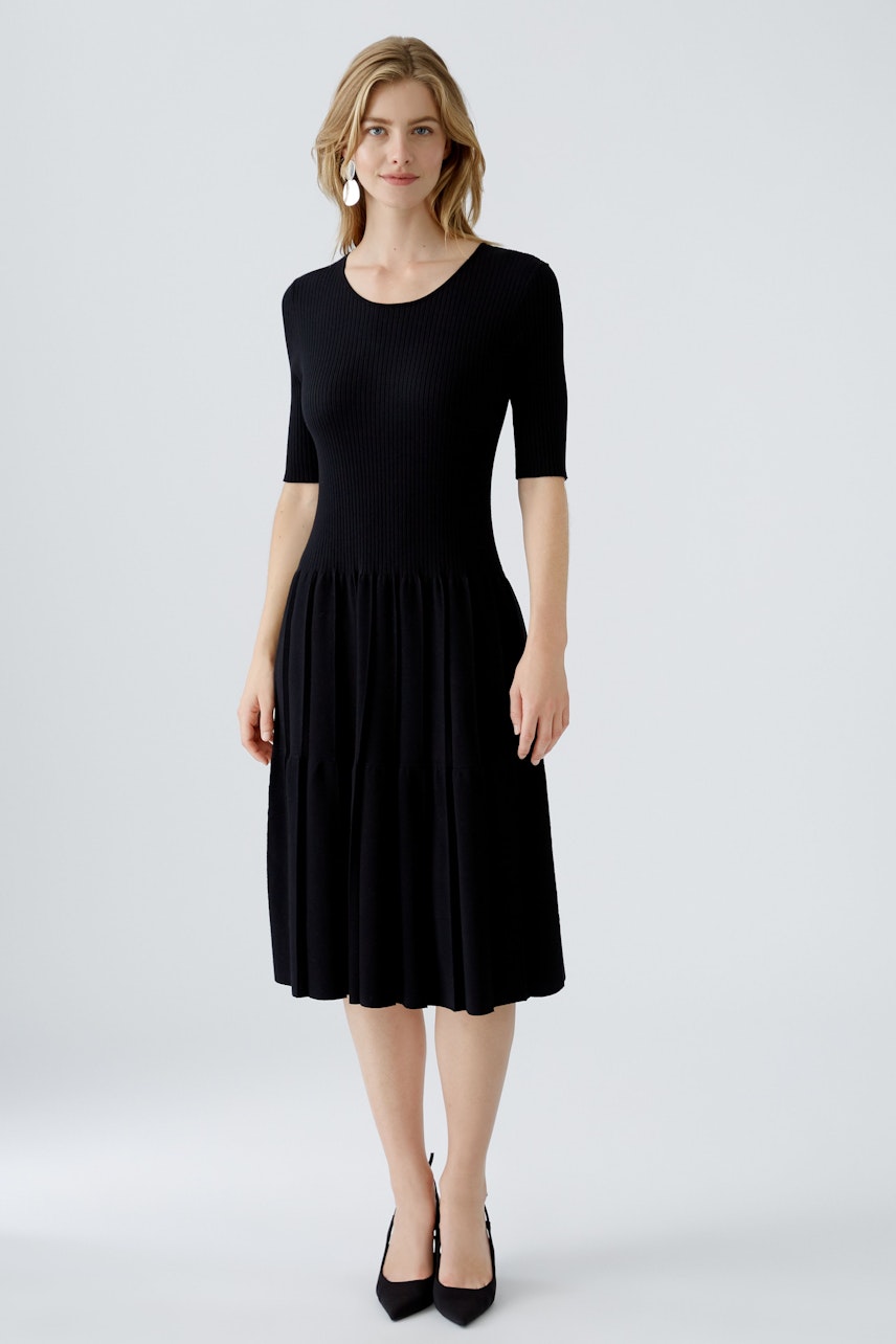 Schwarzes Strickkleid: Frau in einem taillierten, knielangen Kleid mit kurzen Ärmeln und weitem Rock.