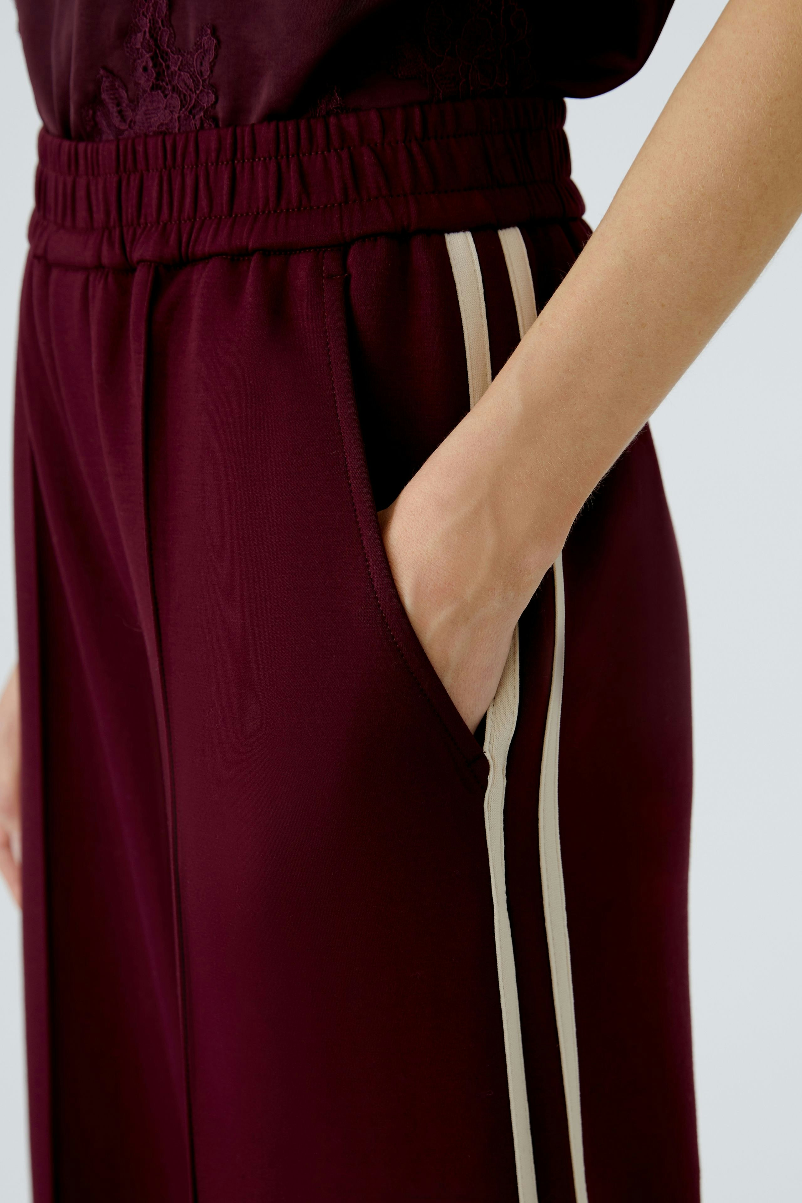Comfortable jogger pants: A woman shows off stylish maroon joggers with side pockets and sporty stripes.