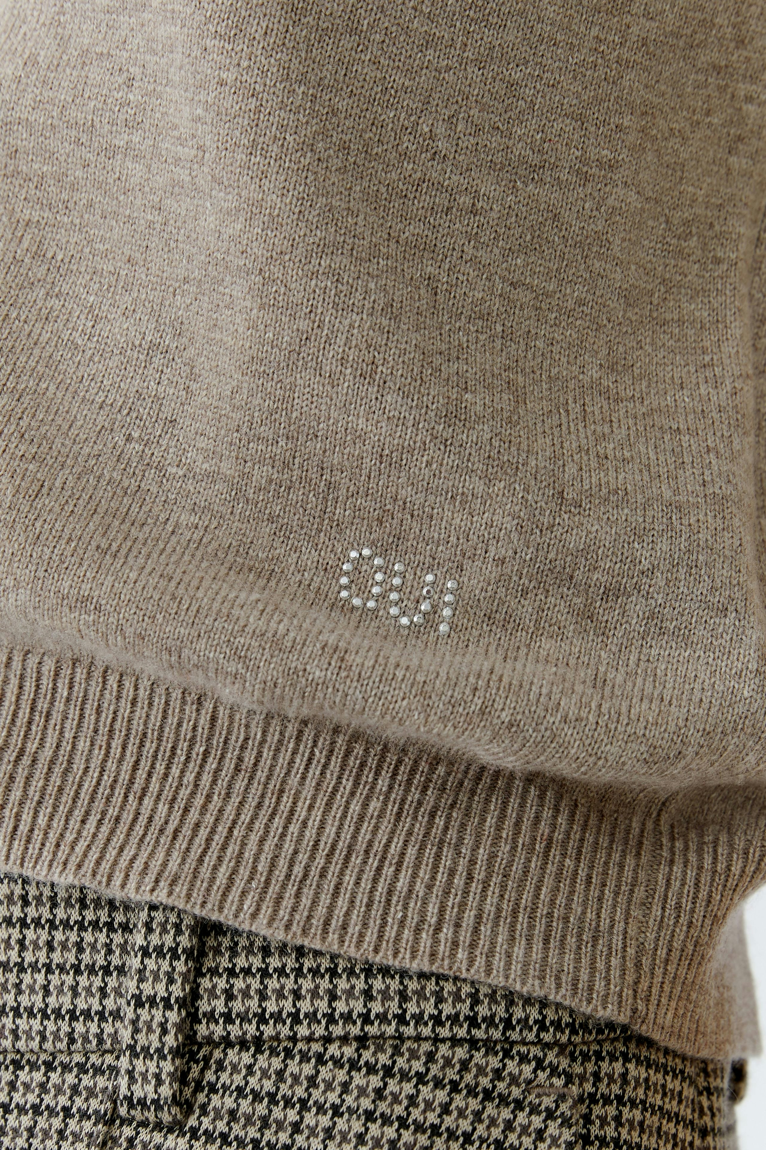 Casual women's pullover in soft beige with subtle logo detail, paired with patterned trousers.