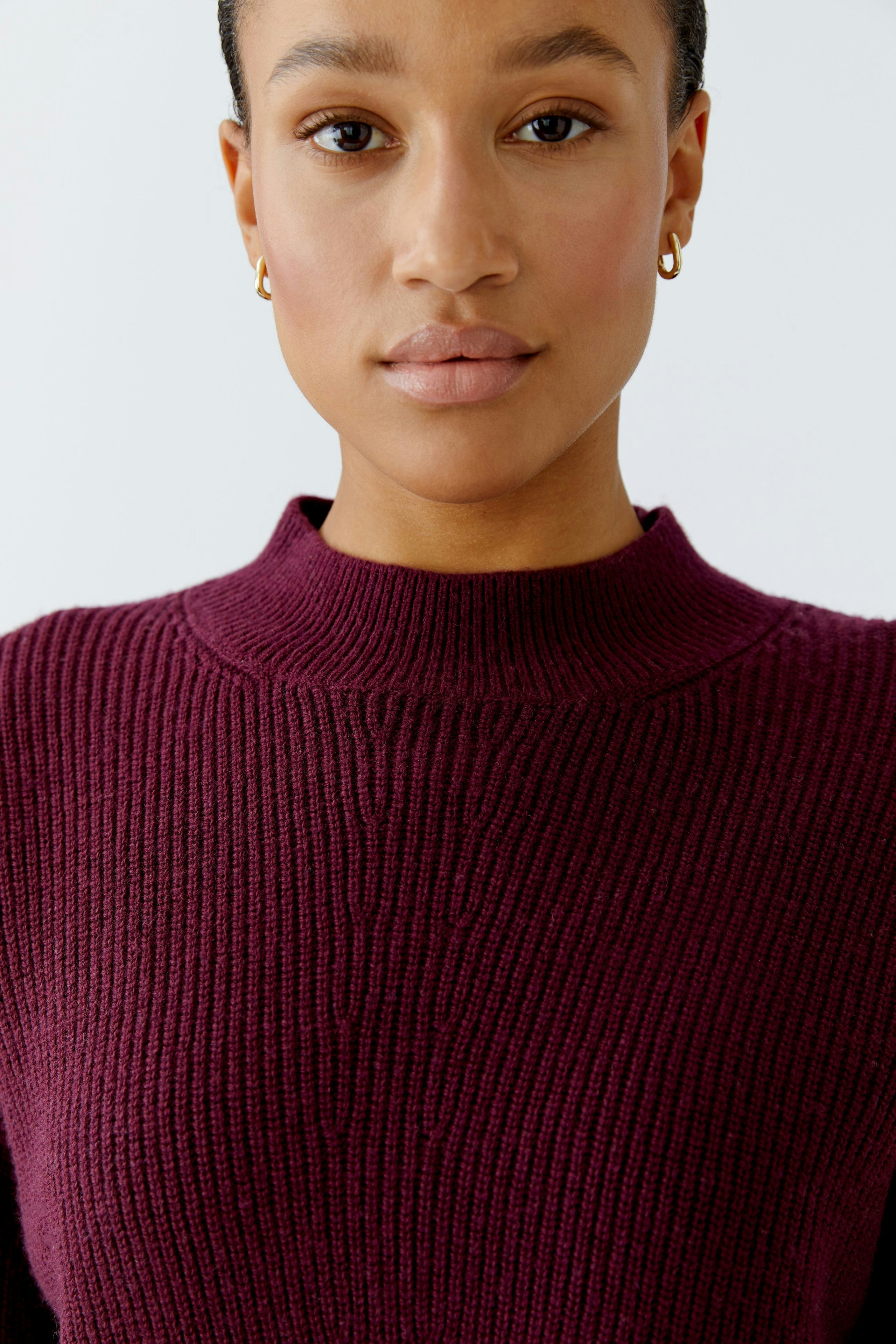Damen-Pullover: Junge Frau im burgunderfarbenen Strickpullover mit hohem Kragen blickt direkt in die Kamera.