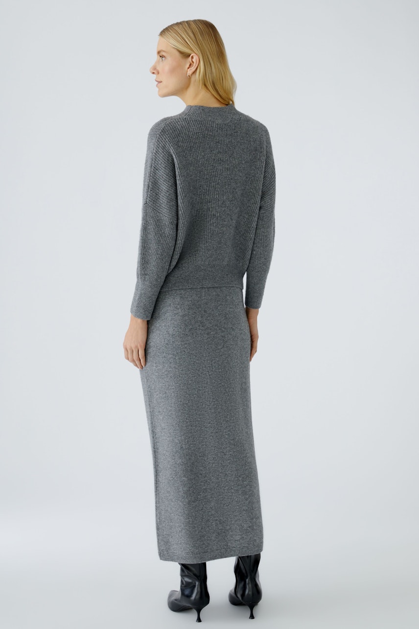 Damen-Pullover: Frau in grauem Strickpullover mit passendem Rock und Stiefeln von hinten.