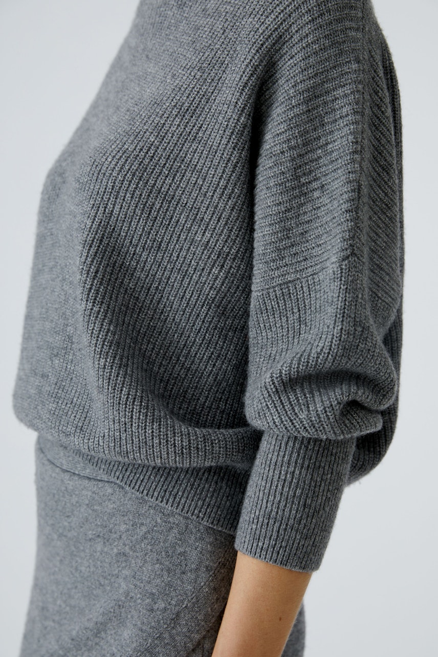Damen-Pullover: Frau in grauem, lässigem Strickpullover mit weitem Schnitt und 3/4-Ärmeln.