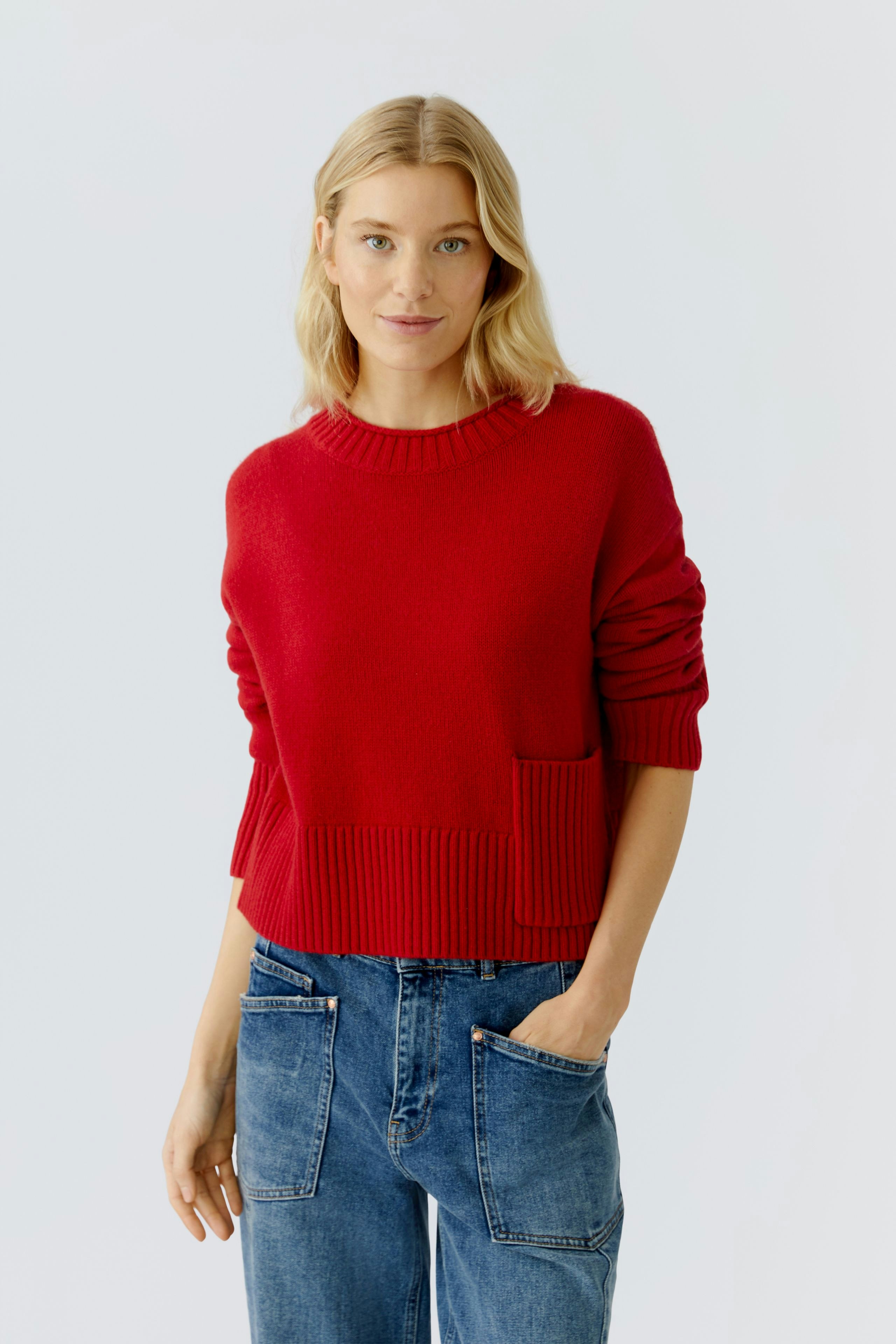 Casual women's pullover: Young woman in a red knit pullover with a pocket, paired with relaxed jeans.