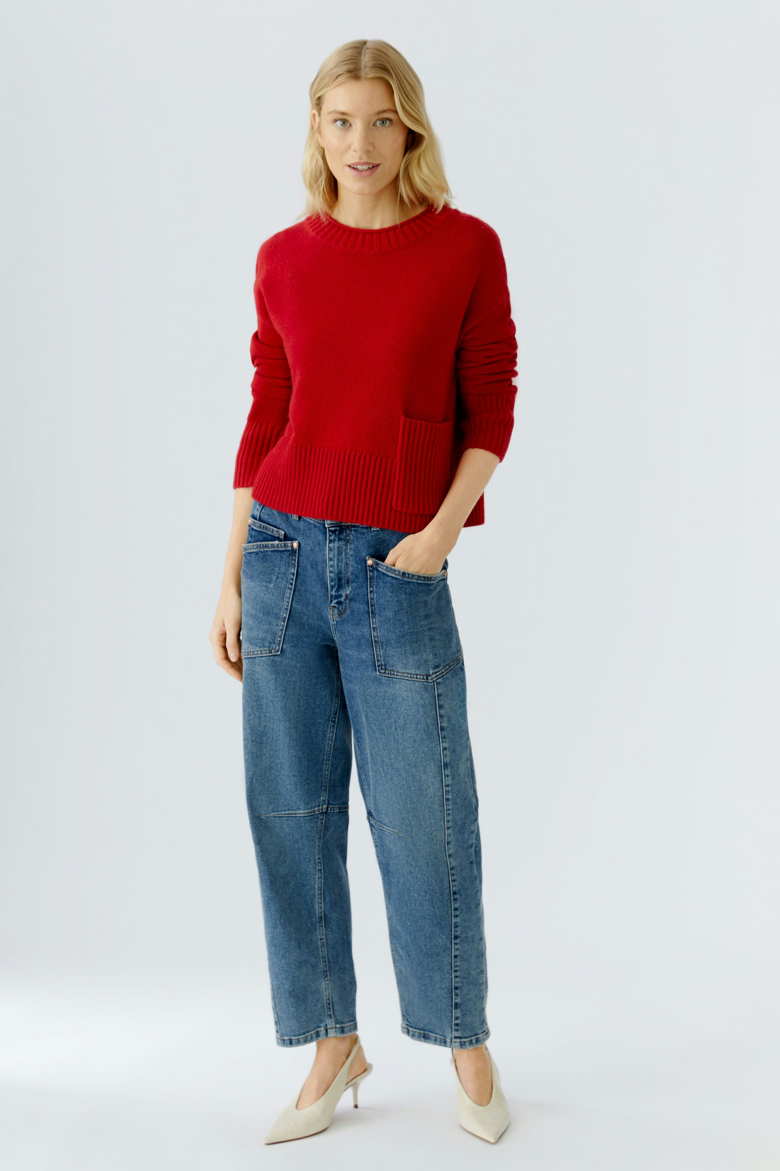 Casual women's pullover: A woman in a red knitted pullover with a pocket, paired with relaxed jeans.