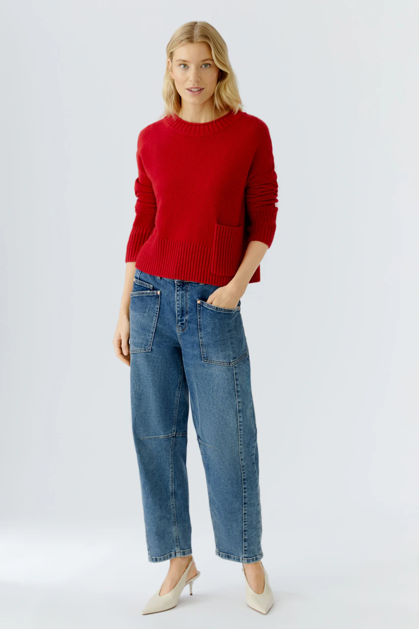 Casual women's pullover: A woman in a red knitted pullover with a pocket, paired with relaxed jeans.