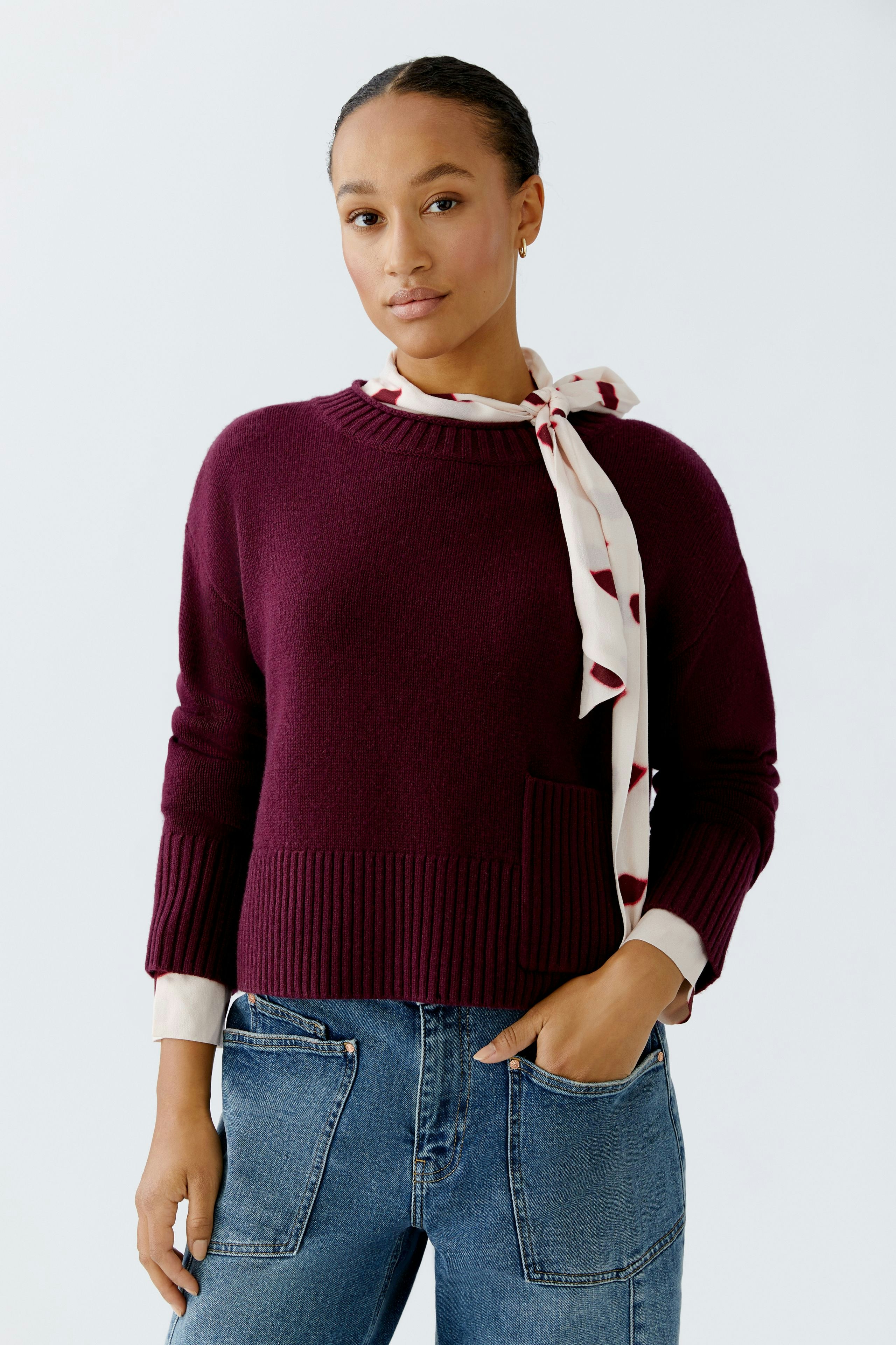 Modern women's pullover: A woman in a burgundy pullover with a pocket and a stylish scarf.
