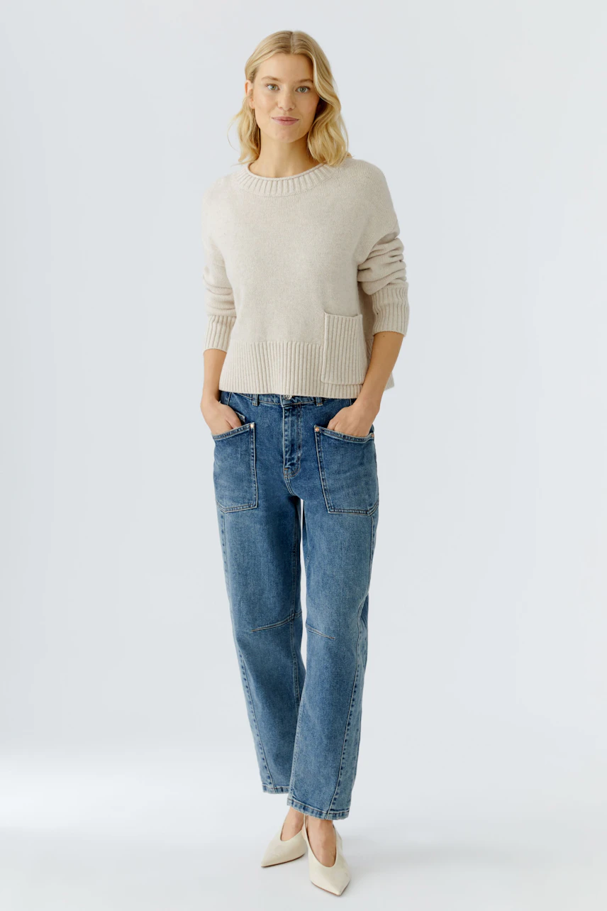 Casual women's pullover: A woman in a light beige pullover with a pocket, paired with relaxed jeans.