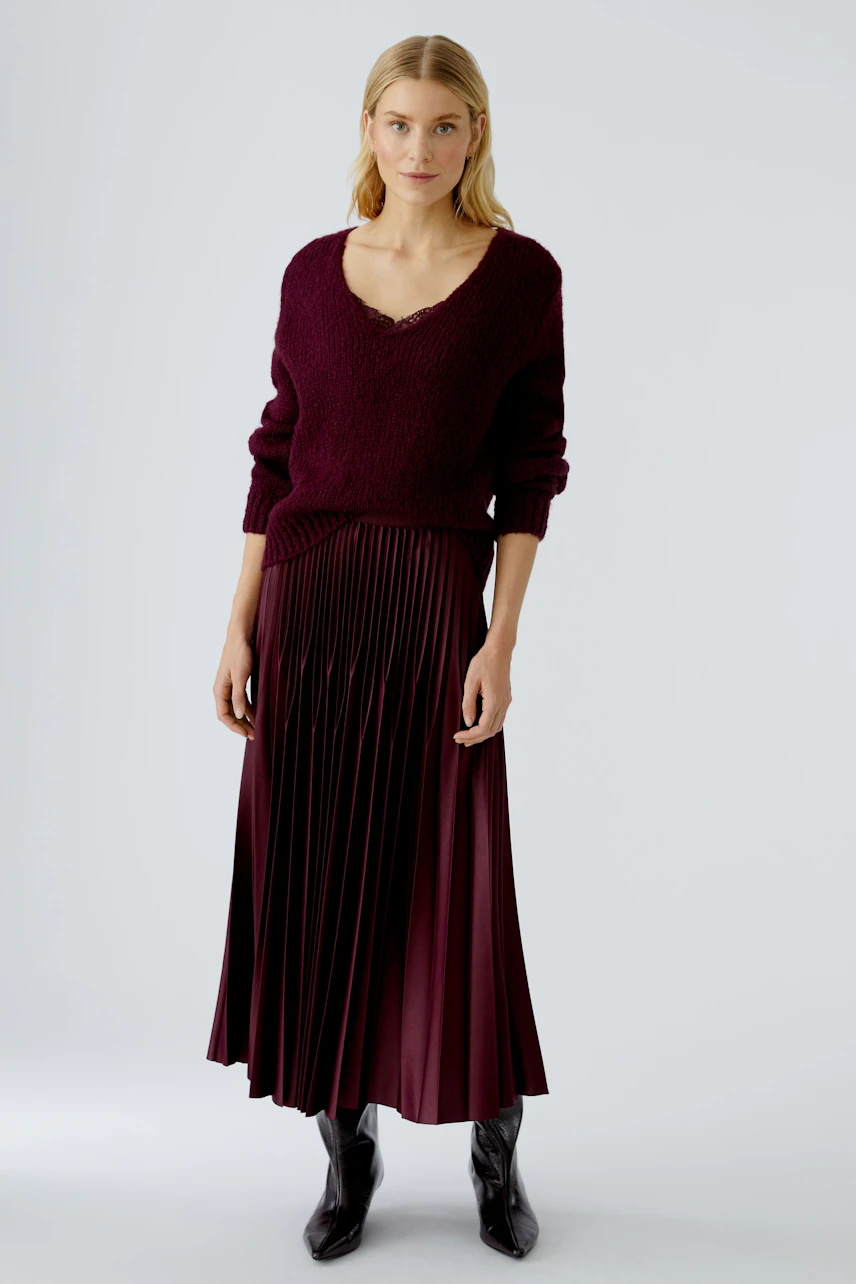 Casual women's pullover: Young woman in a burgundy knit pullover with a V-neck, paired with a pleated skirt.