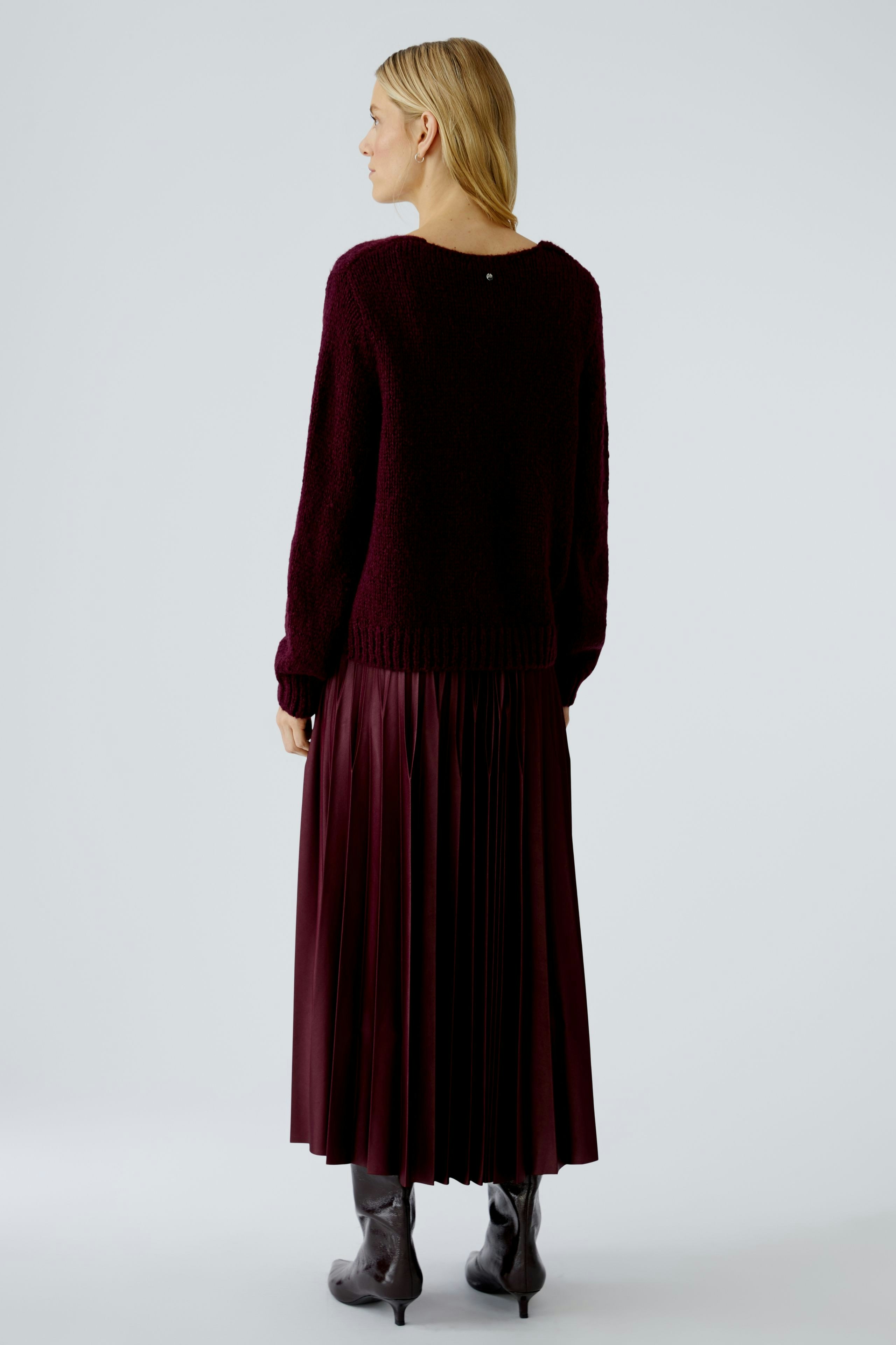 Casual women's pullover: A woman in a burgundy knit pullover paired with a pleated skirt.