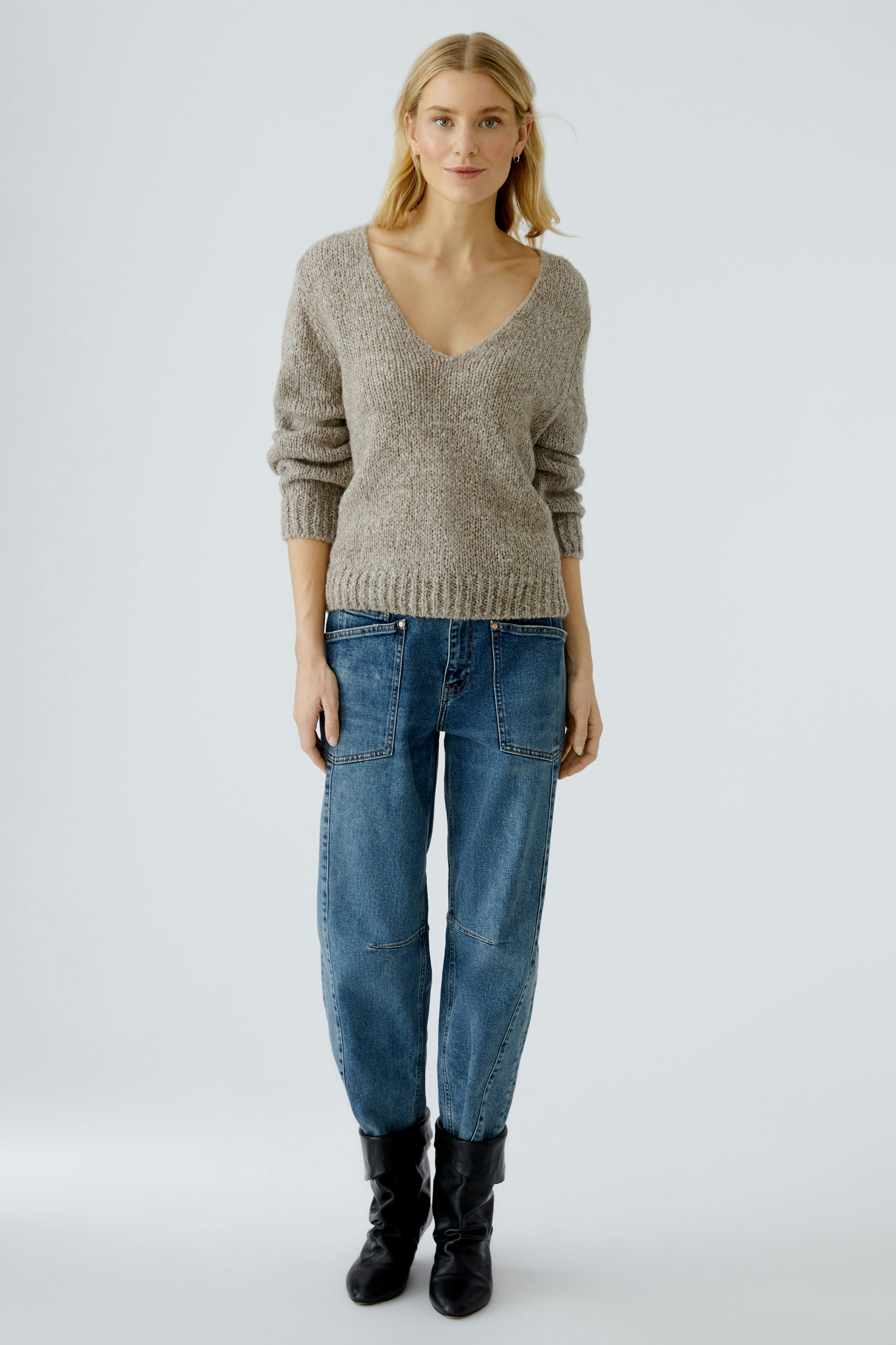 Casual women's pullover: Young woman in a cozy beige V-neck pullover paired with relaxed jeans.
