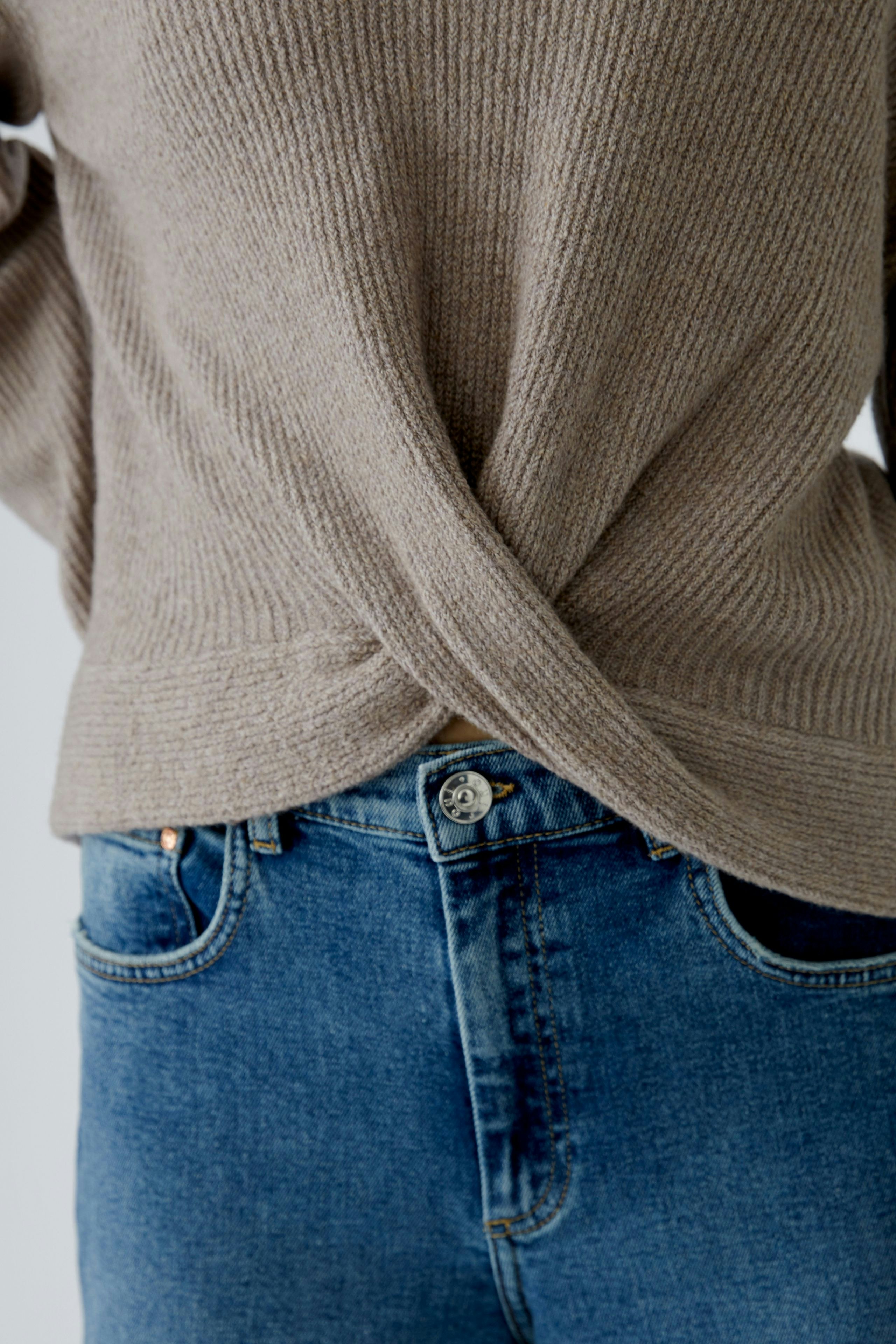 Casual women's pullover: A woman in a beige ribbed pullover with a stylish twist detail at the back.