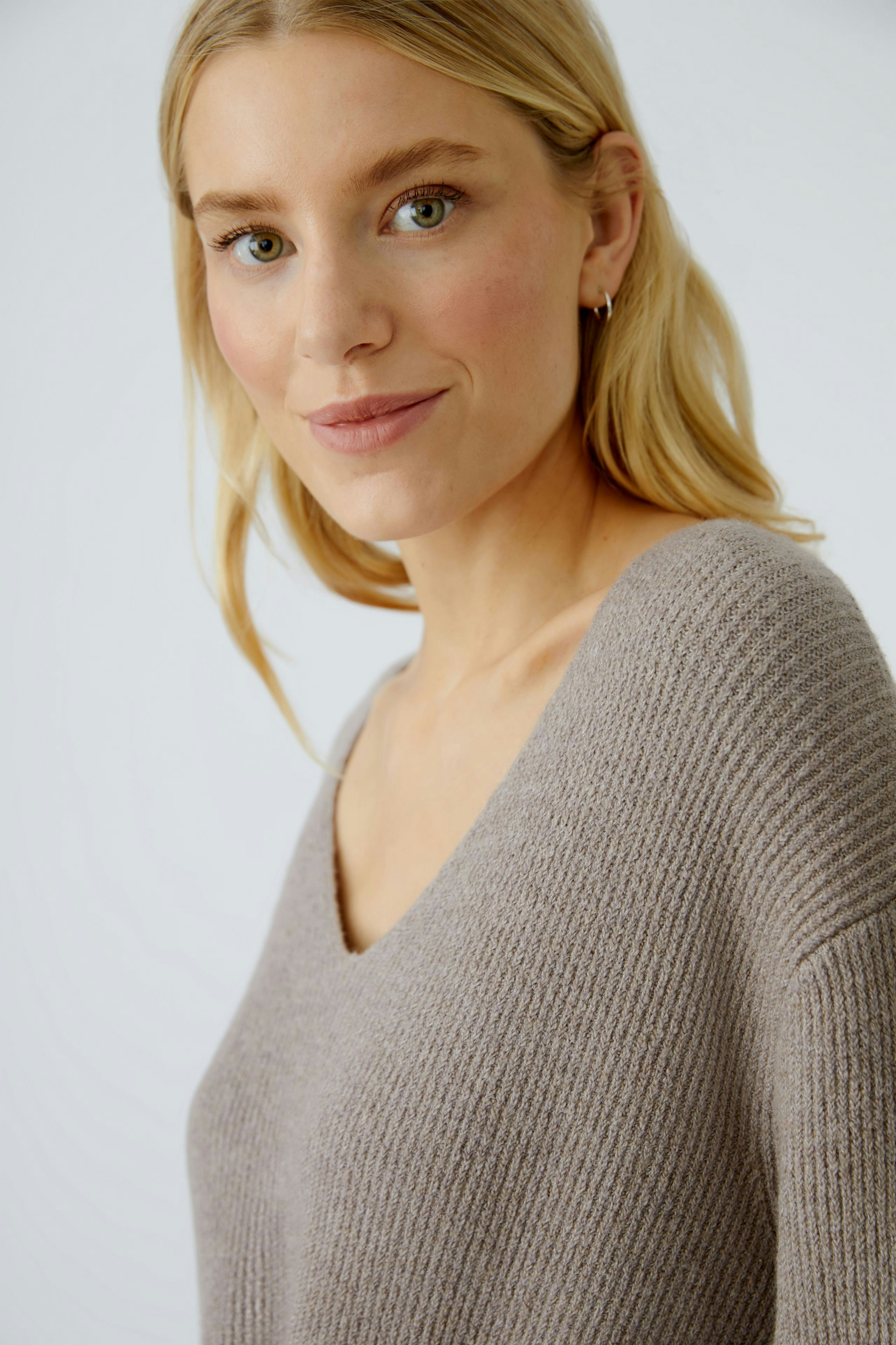 Casual women's pullover: Young woman in a soft, light brown V-neck pullover, smiling confidently.