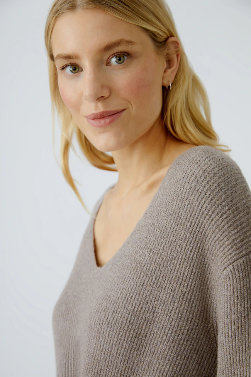 Casual women's pullover: Young woman in a soft, light brown V-neck pullover, smiling confidently.