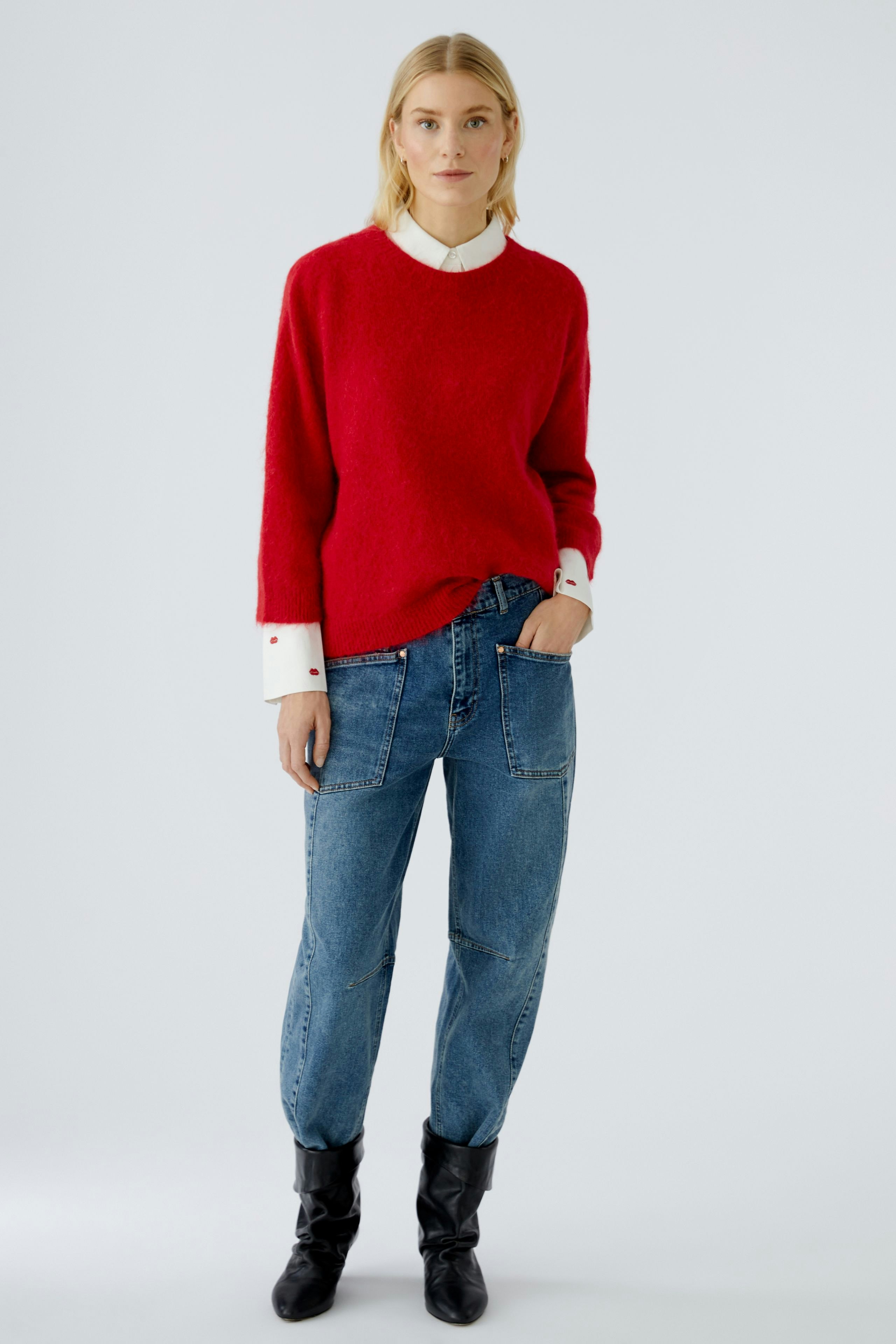 Casual women's pullover: Young woman in a red pullover over a white shirt, paired with relaxed jeans.