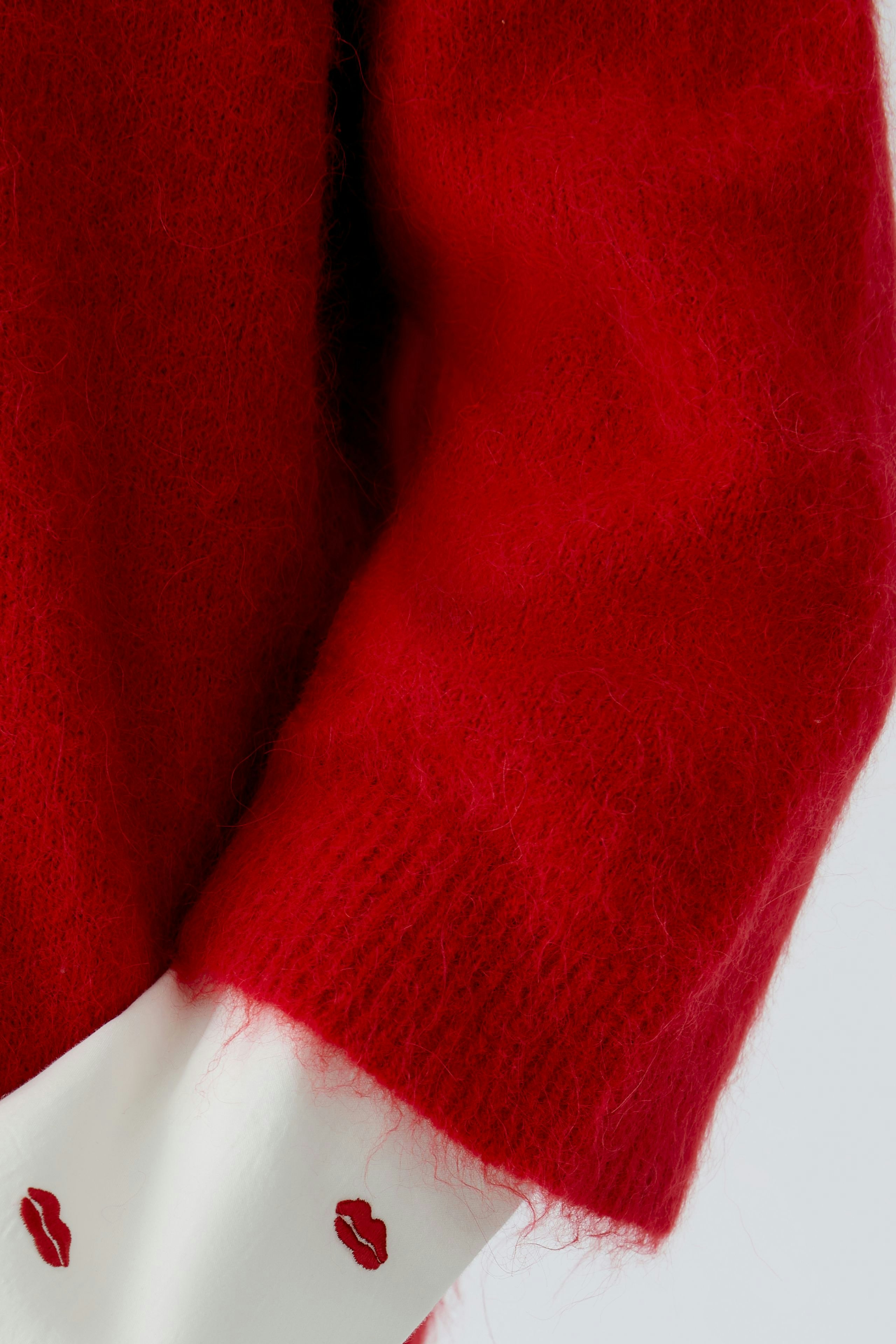 Cozy red pullover with soft texture and playful lip print detail on the sleeves.