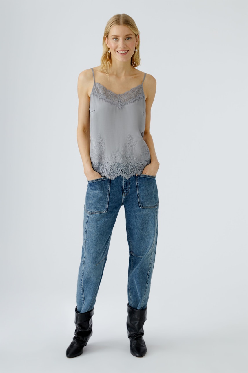 Leichtes Damen-Top in Grau mit Spitzenbesatz, kombiniert mit lässigen Jeans und Stiefeln.