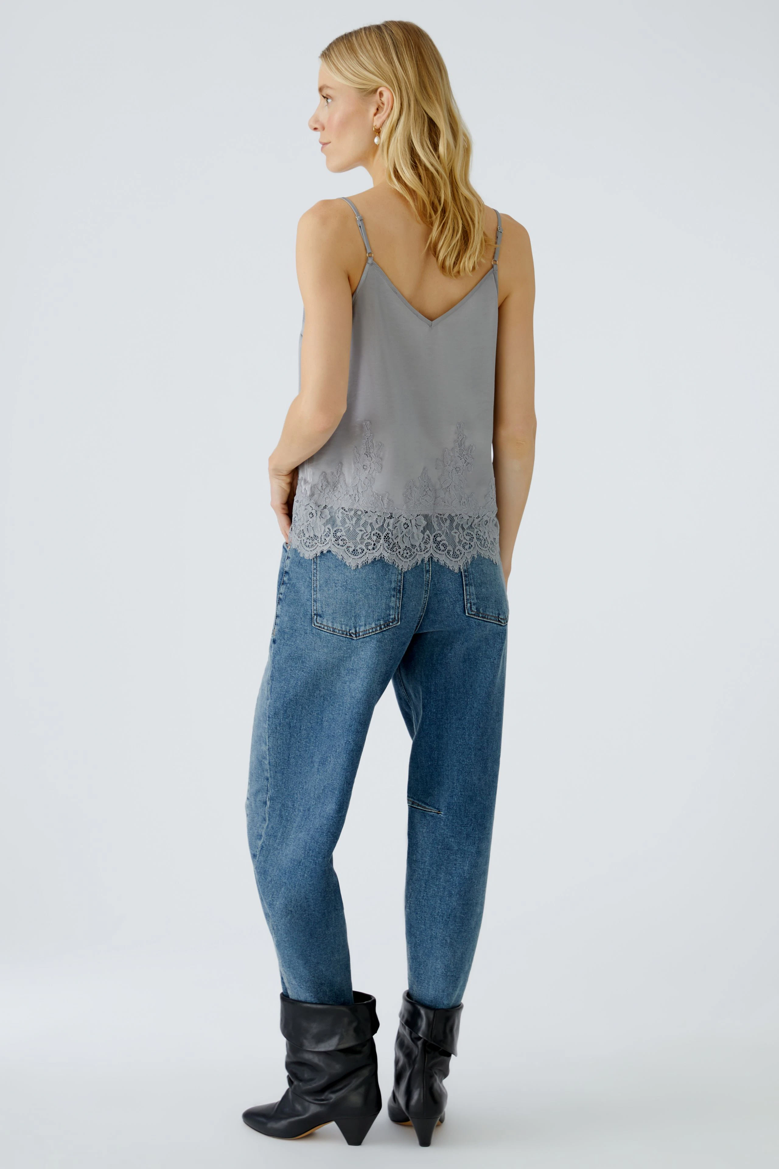Damen-Top: Junge Frau trägt ein graues Top mit Spitzenbesatz und lässigen Jeans.