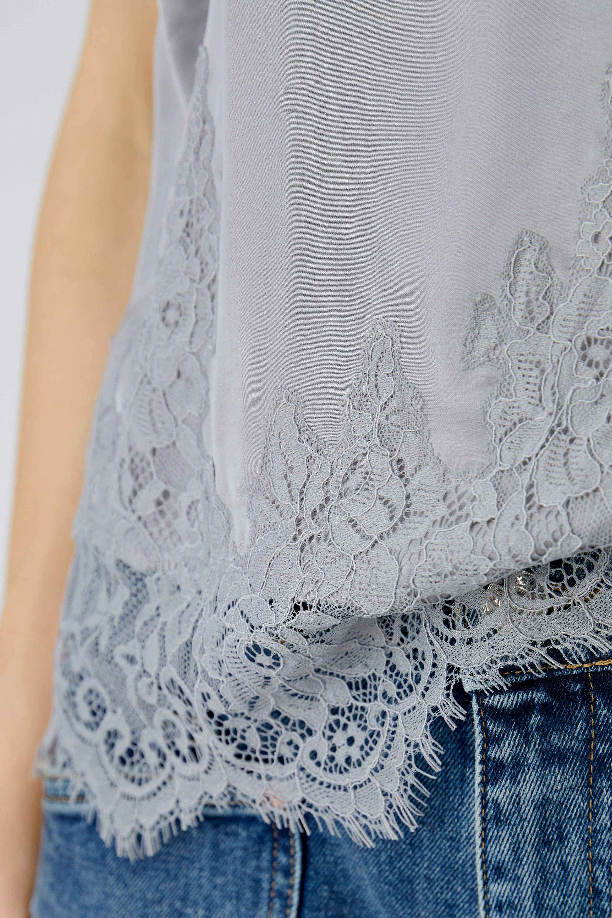 Damen-Top: Junge Frau trägt ein graues Top mit Spitzenbesatz am Ausschnitt und lässigem Look.