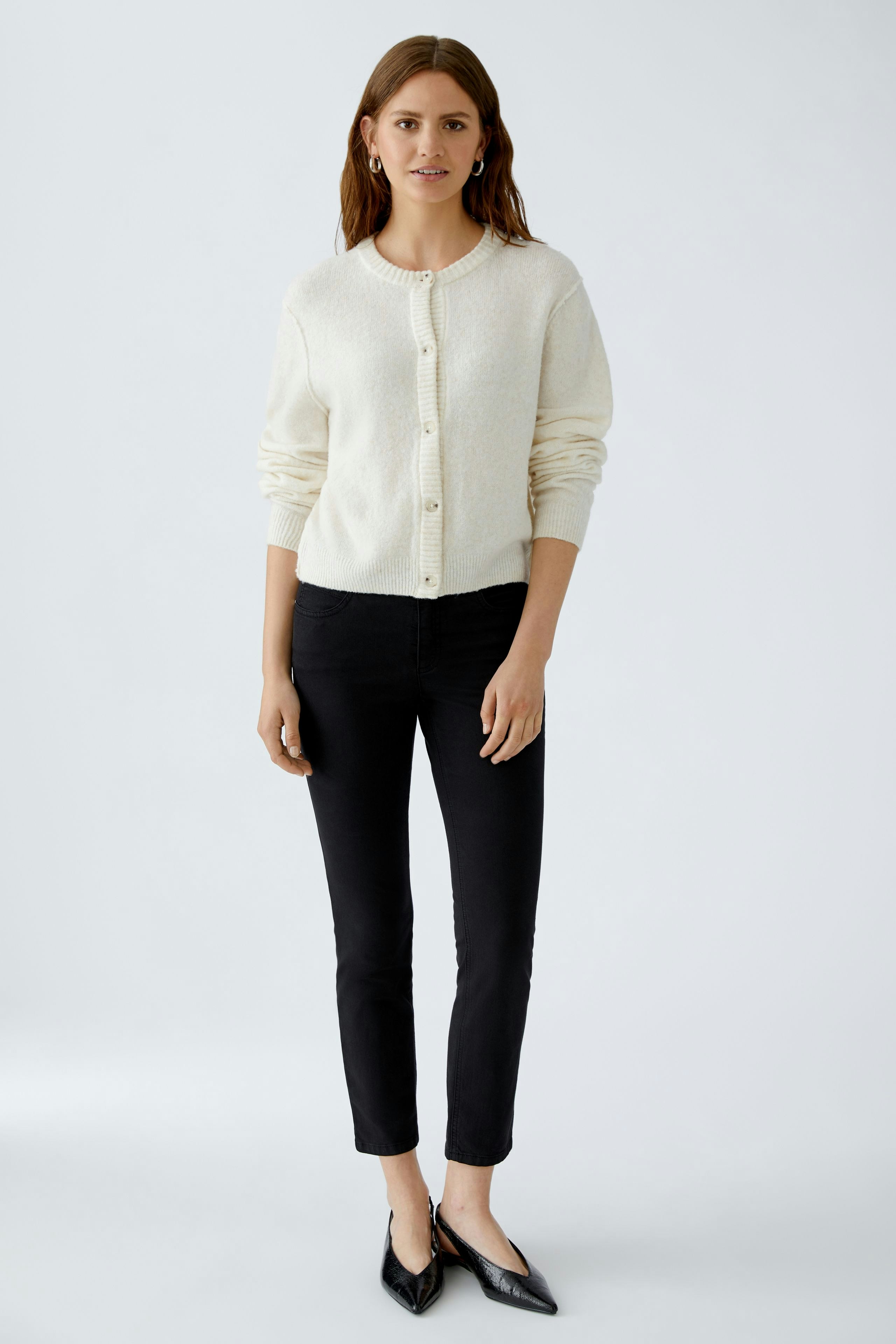 Damen-Strickjacke: Frau in cremefarbener Strickjacke mit Knöpfen und schwarzen Jeans steht lässig.
