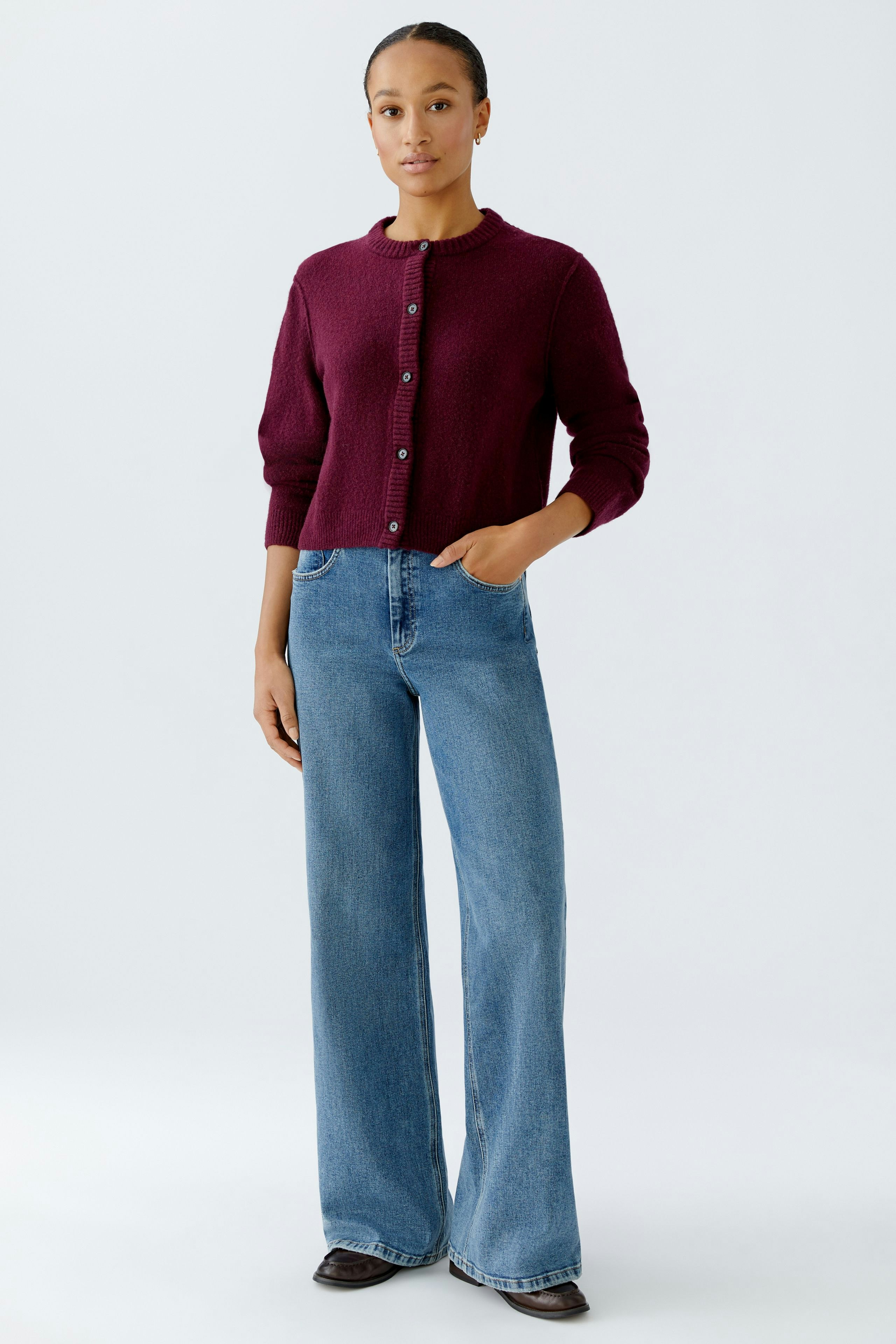 Casual women's cardigan: A woman in a burgundy cardigan with buttons, paired with wide-leg jeans.