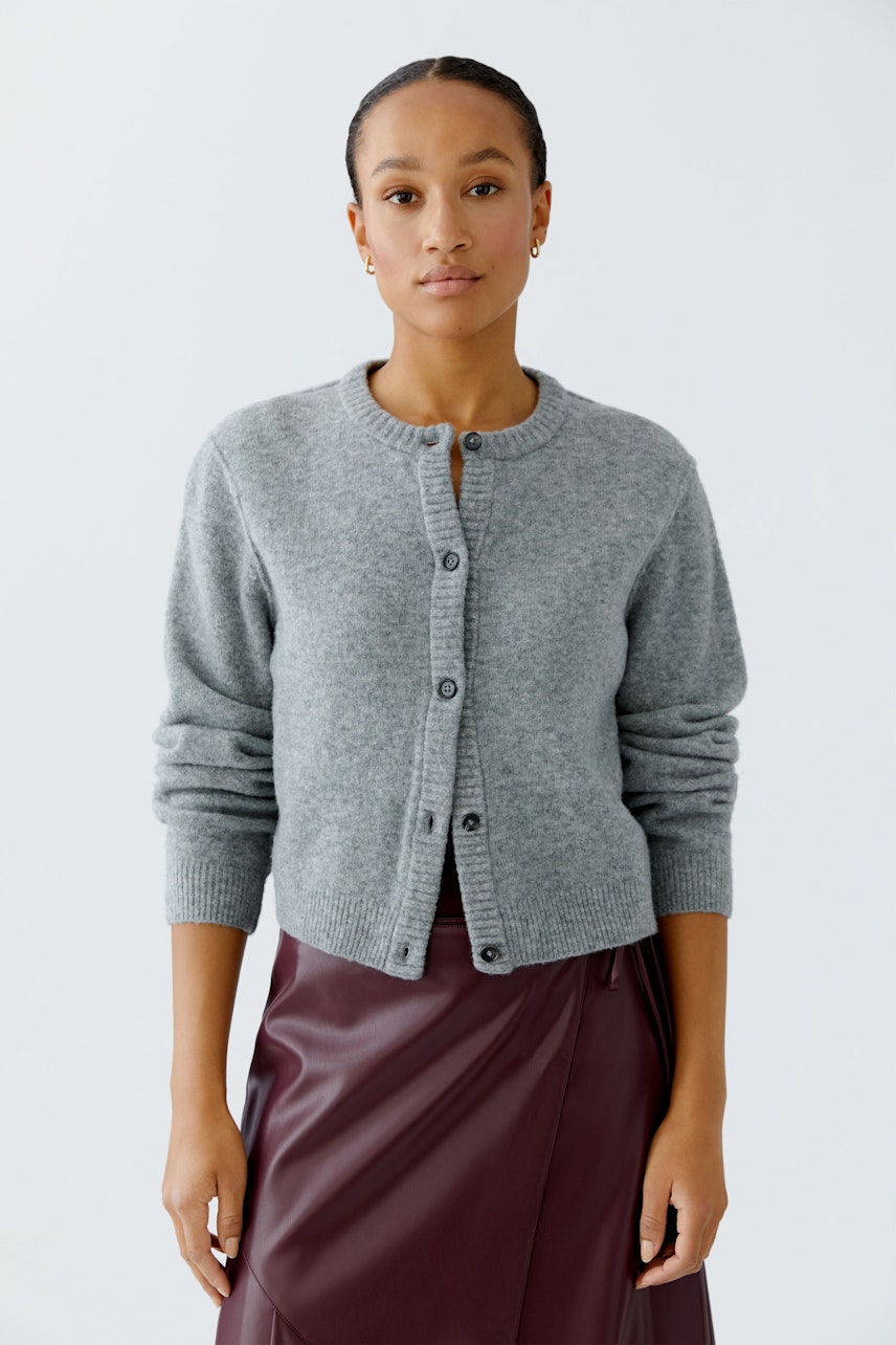 Damen-Strickjacke: Frau in grauer Strickjacke mit Knöpfen und lässigem Rock.
